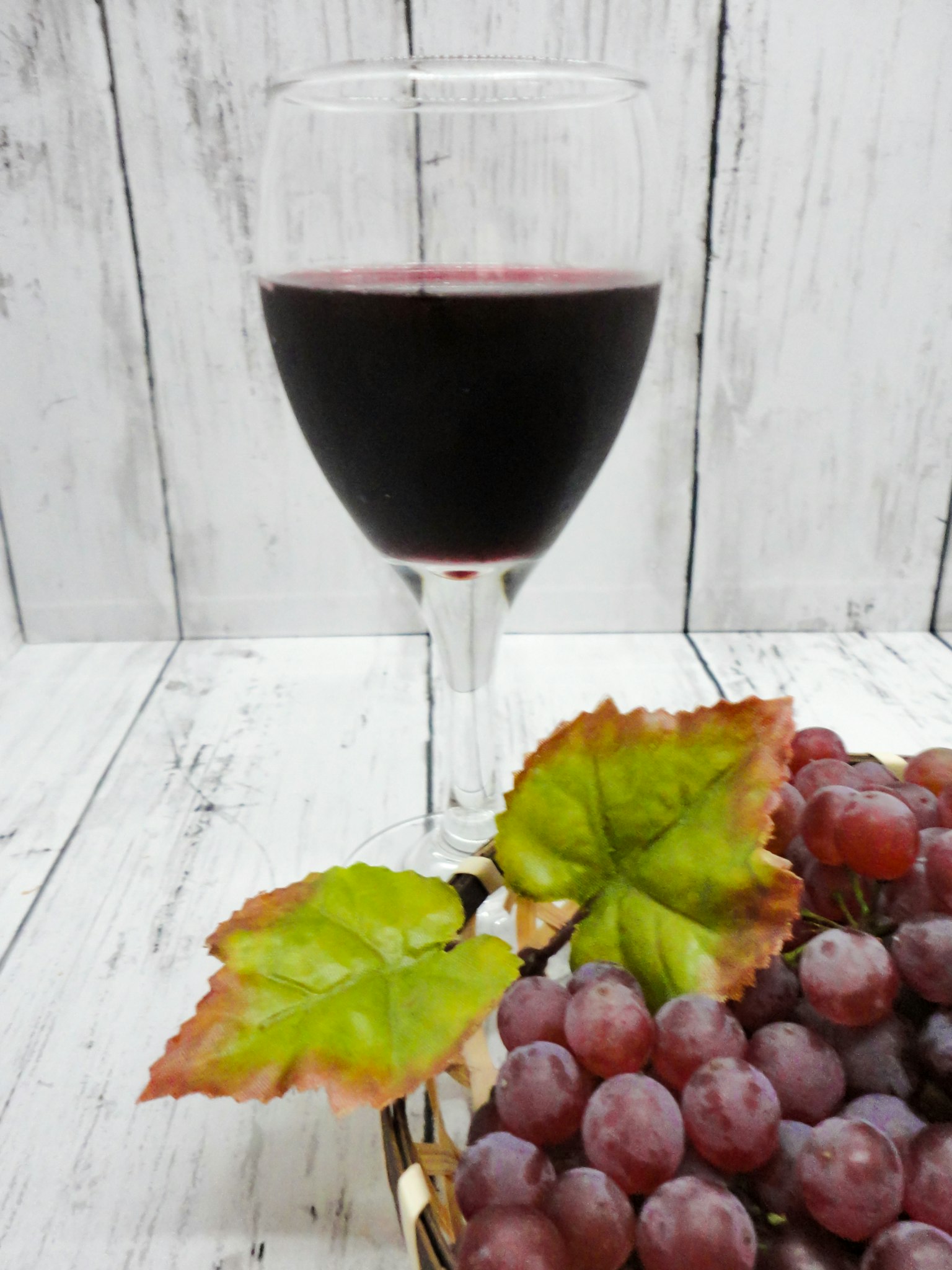 Ein Glas Rotwein neben einem Traubenstrauß mit grünen Blättern