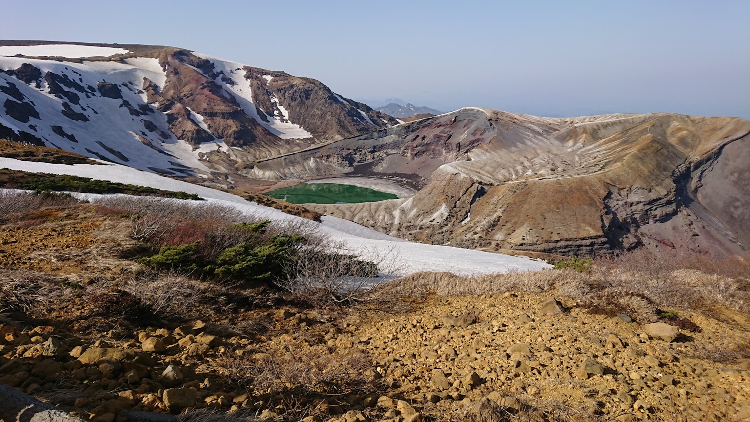 Panoramaansicht von Bergen mit verbleibendem Schnee und einem grünen See