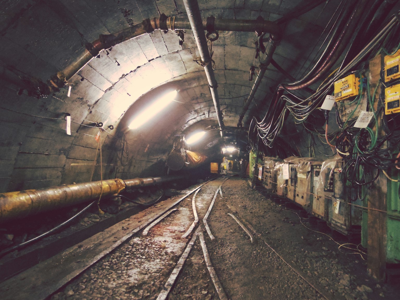 Interno di un tunnel buio con binari ferroviari e pannelli elettrici