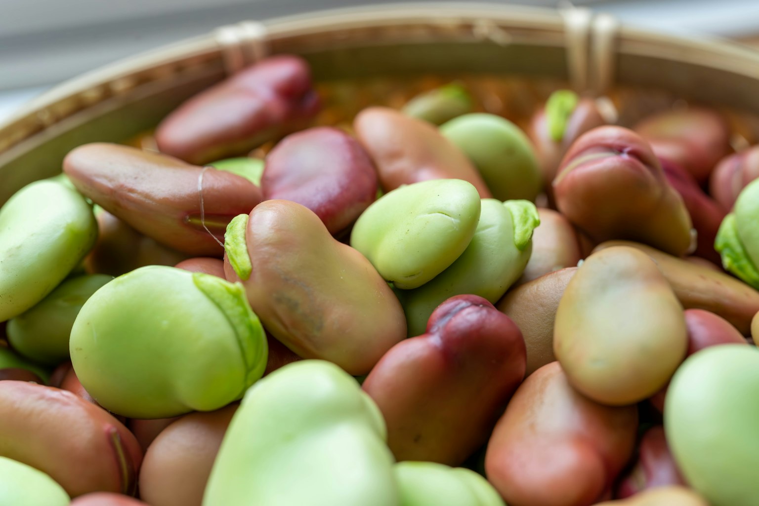 Gros plan de haricots verts et brun rougeâtre dans un panier en bambou