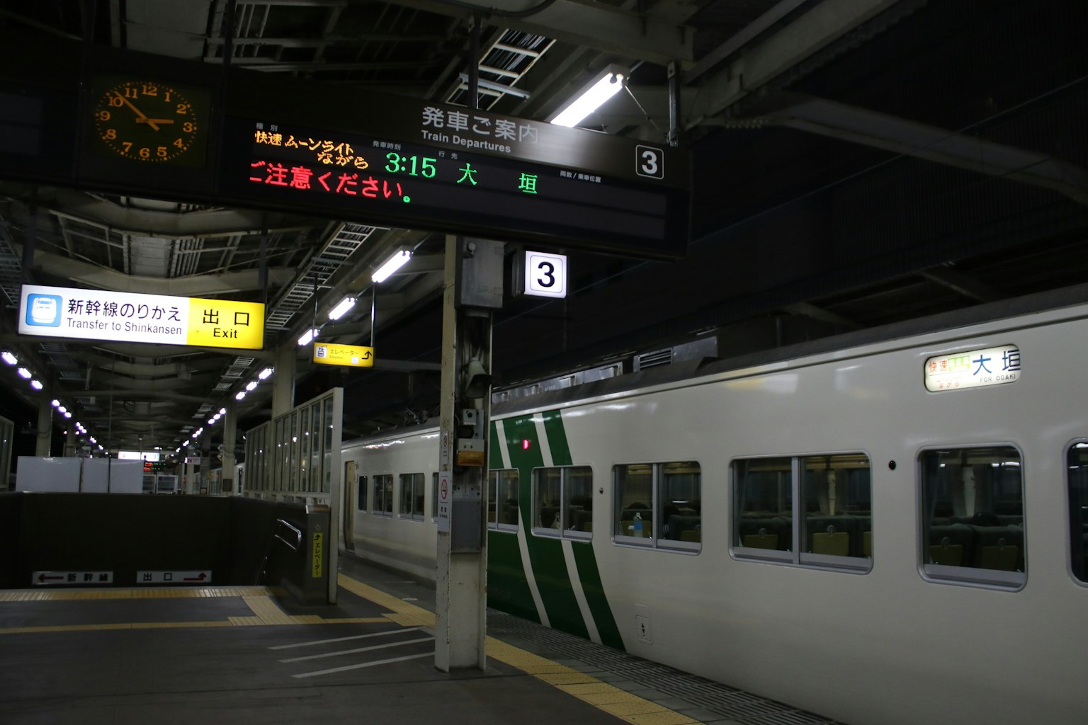 รถไฟลายเขียวที่สถานีตอนกลางคืนพร้อมป้ายแสดงผล