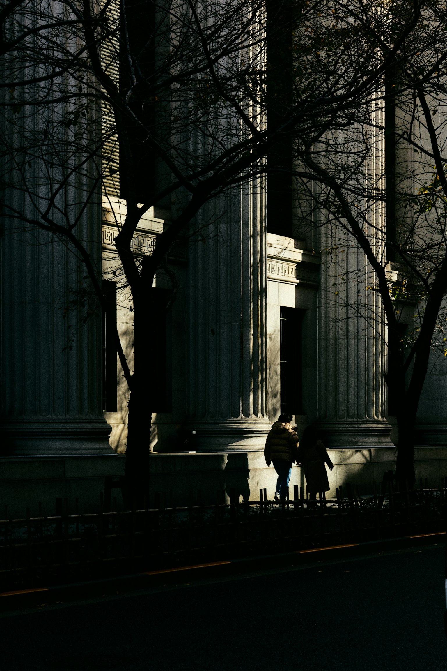 Silhouetted people standing near large architectural columns in shadow