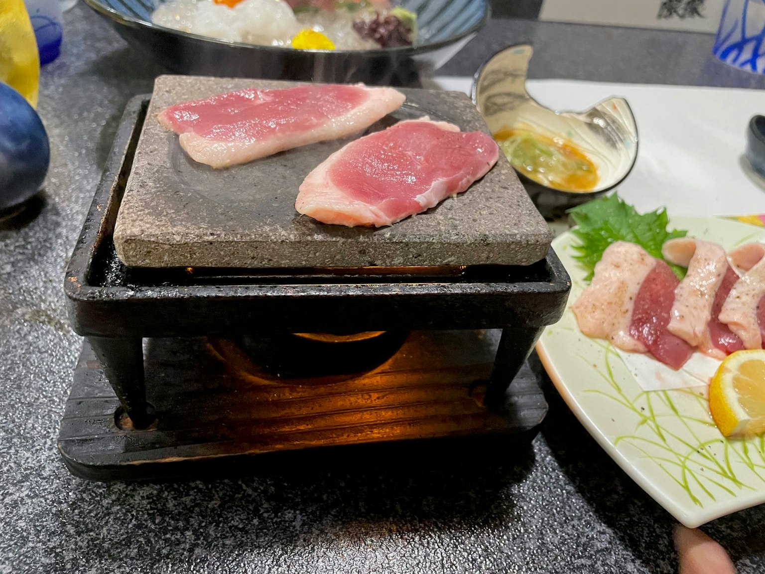 Sliced meat on a hot stone grill with surrounding dishes