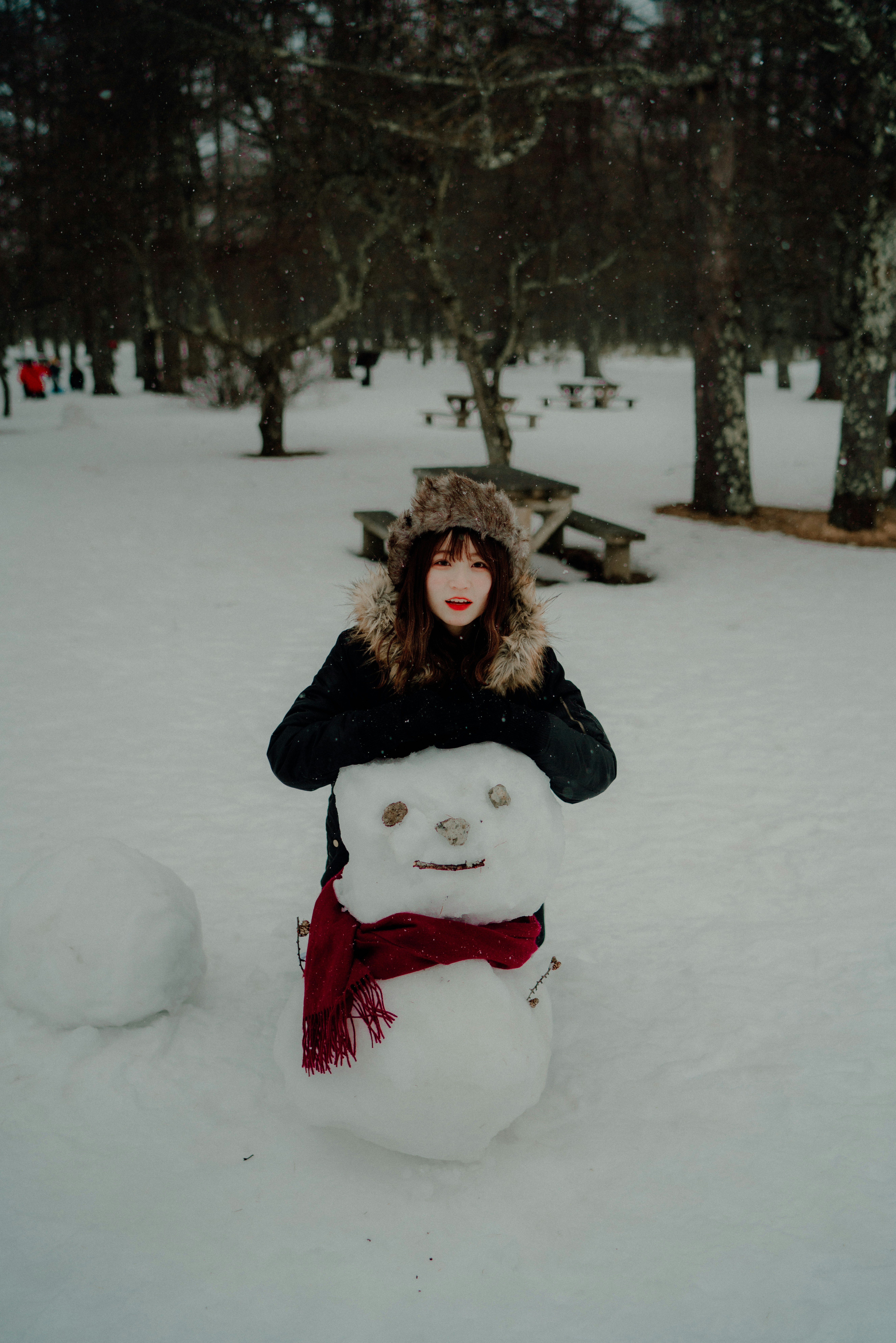 雪の公園で雪だるまと一緒に立つ女性の冬のスナップ