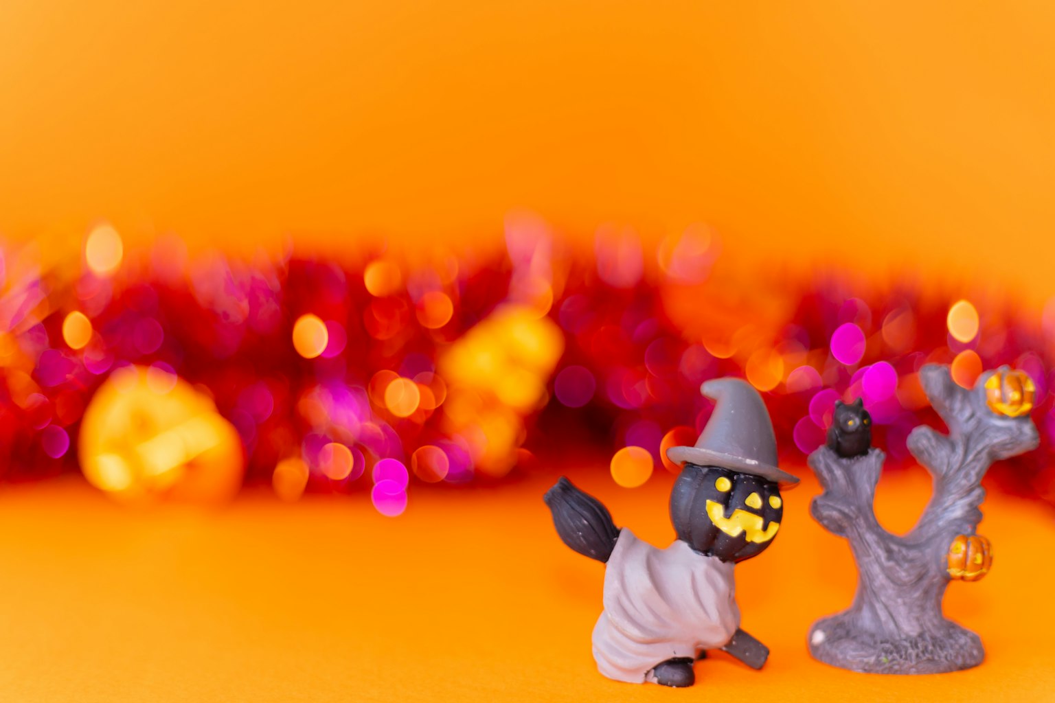 Immagine a tema Halloween con una figurina di gatto nero che indossa un cappello da strega su sfondo arancione