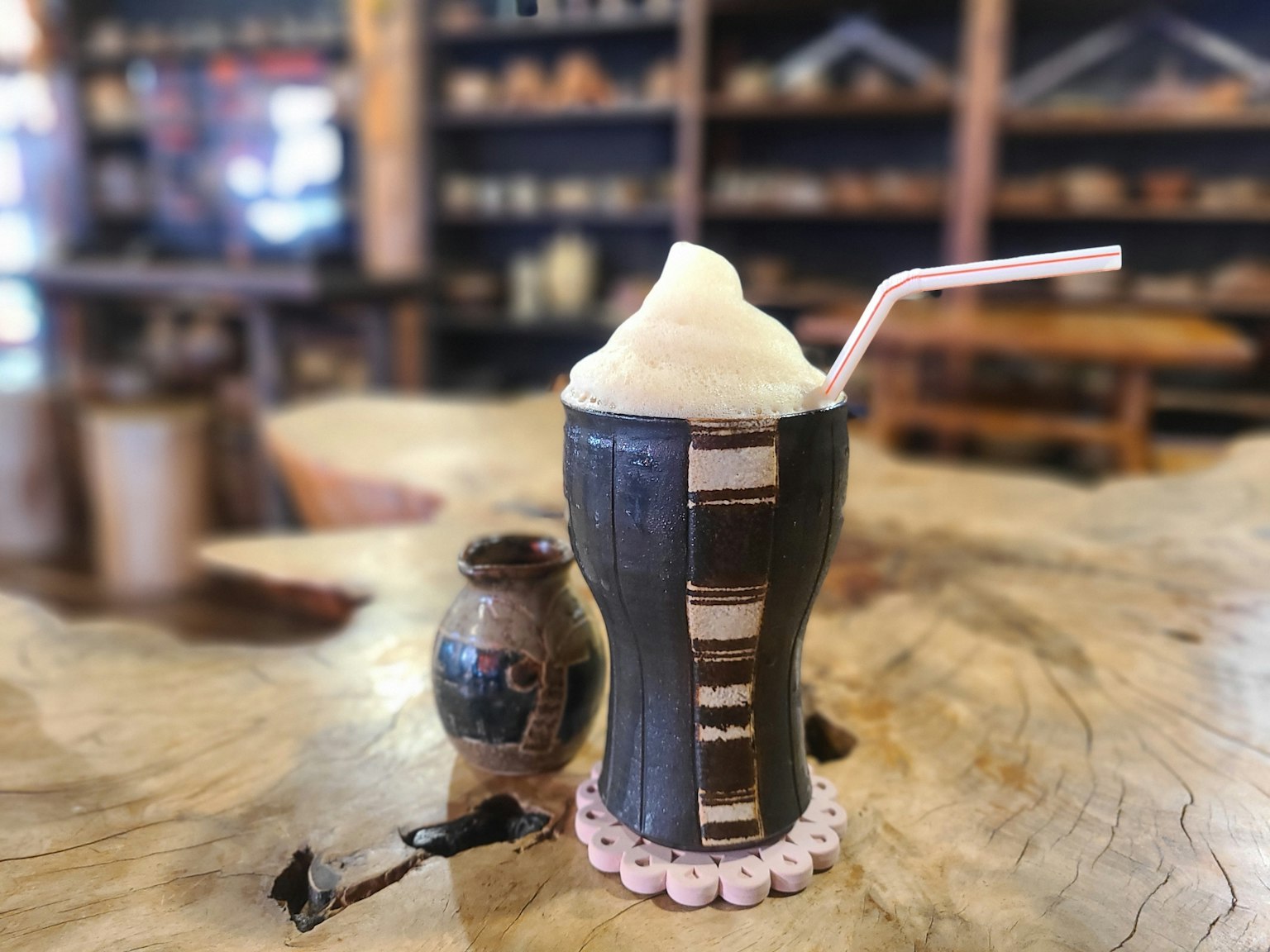 Minuman berbusa dalam cangkir dekoratif di atas meja kayu dengan kendi keramik kecil