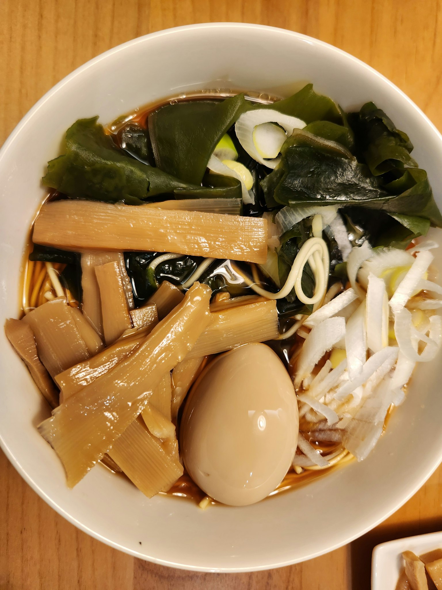 Una ciotola di ramen con germogli di bambù, uovo sodo, alga e cipolle verdi
