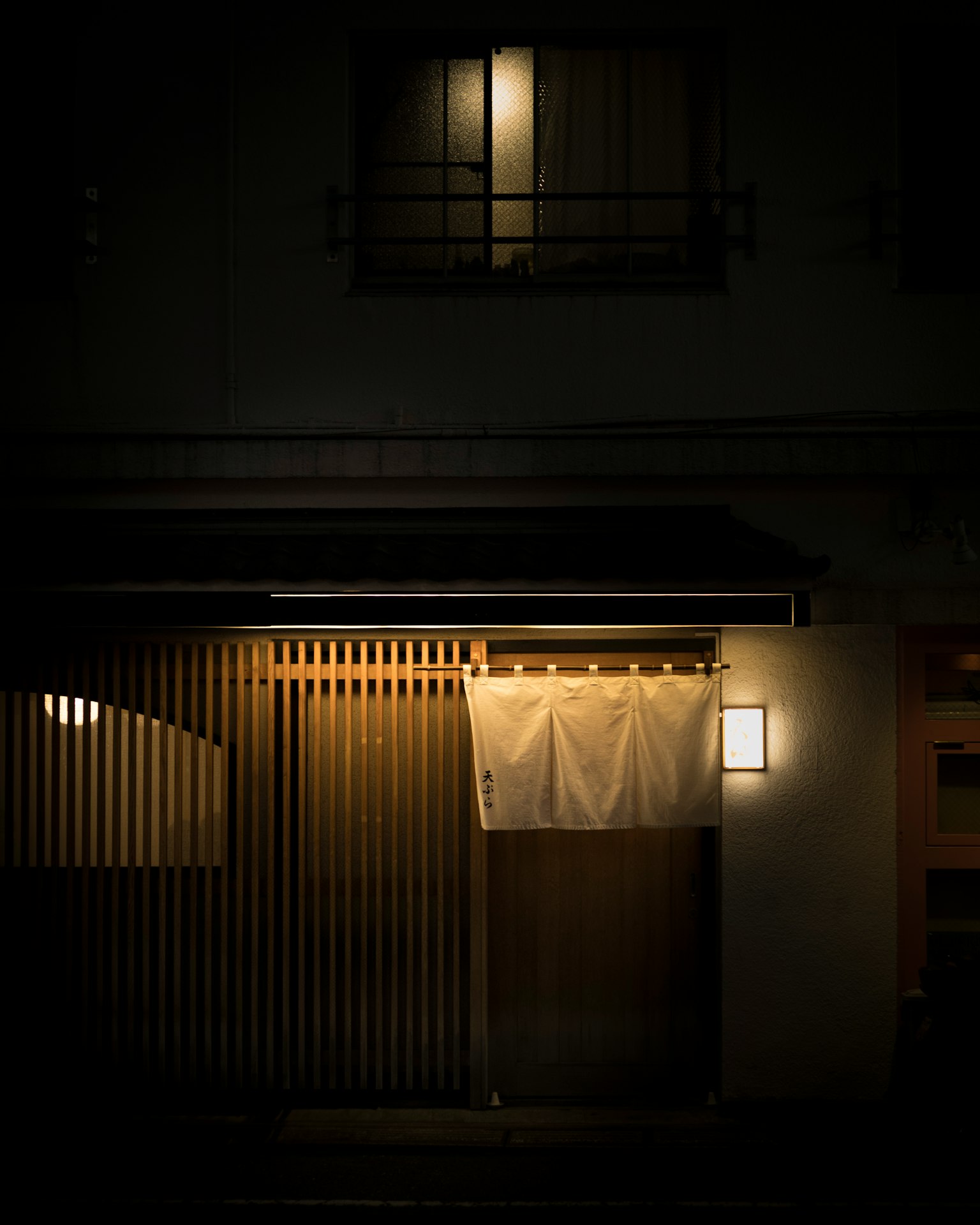 暗い通りにある和風のレストランの入り口 照明が温かくて落ち着いた雰囲気 白い暖簾がかかっている