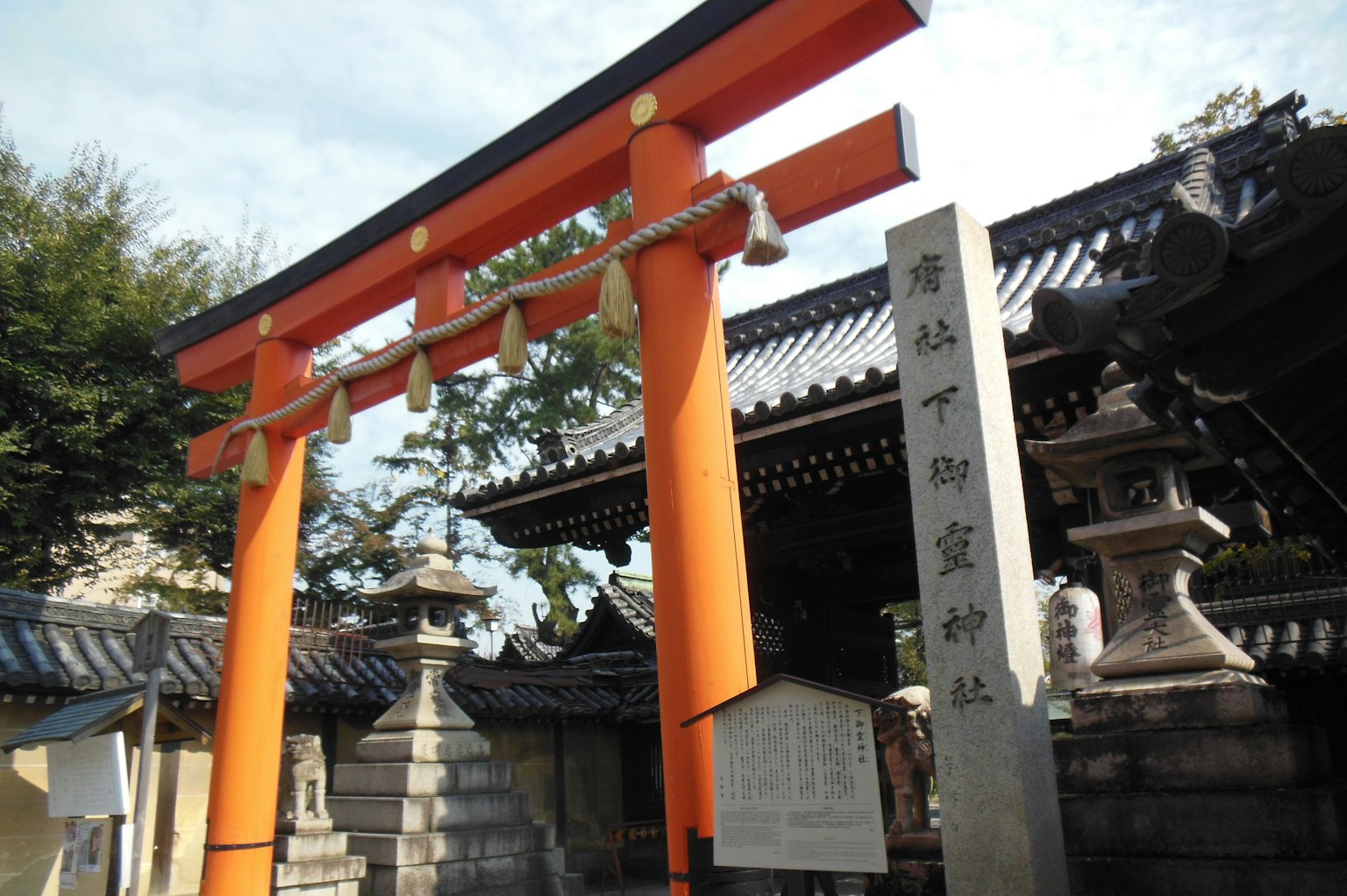 Eingang eines japanischen Schreins mit einem orangefarbenen Torii und einem Steindenkmal