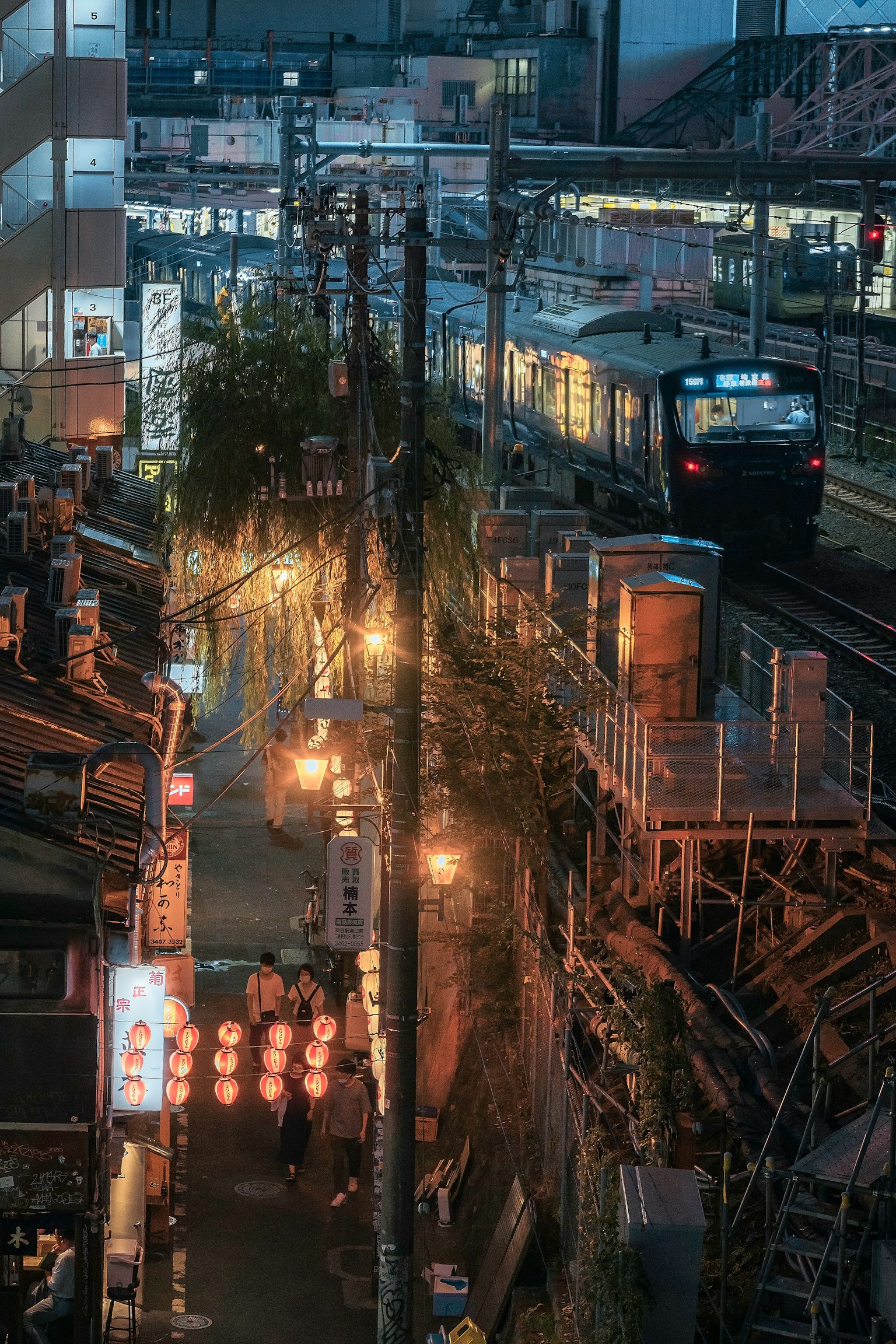Vue nocturne d'une rue japonaise avec des lanternes et des établissements de restauration le long des voies ferrées alors qu'un train passe