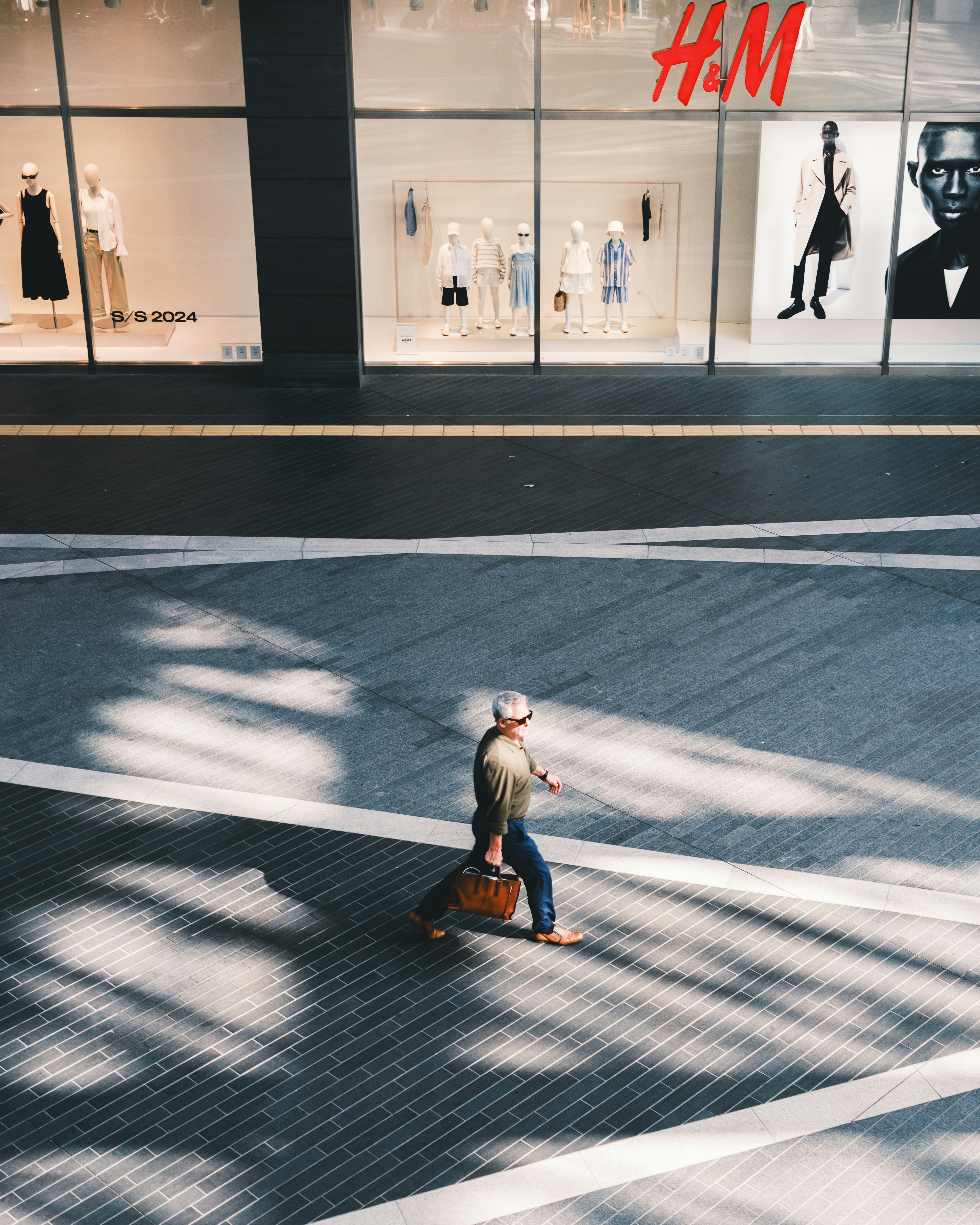person walking in front of a glass storefront with an H&M window display