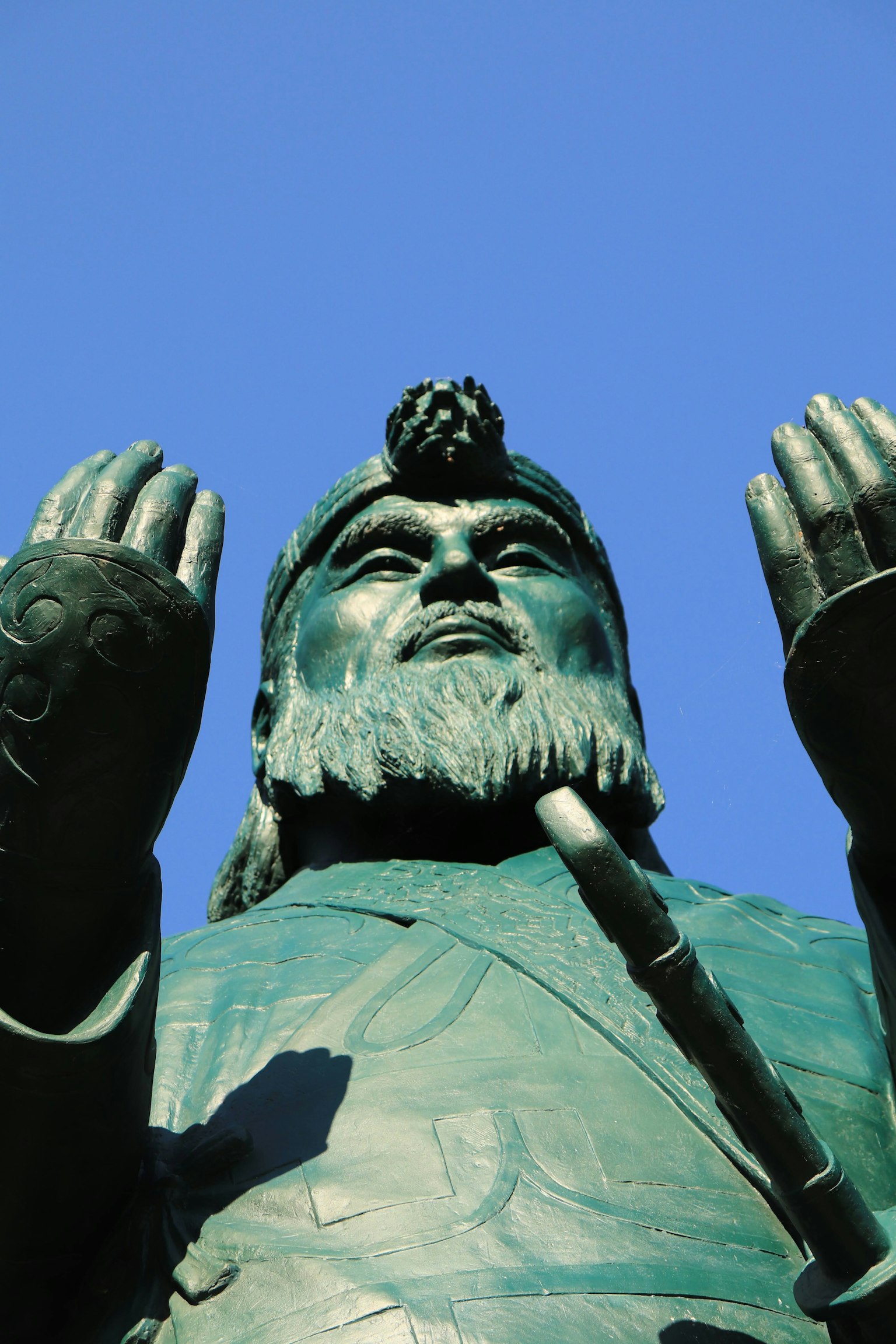 Große bronzene Statue einer Figur mit erhobenen Händen unter einem blauen Himmel
