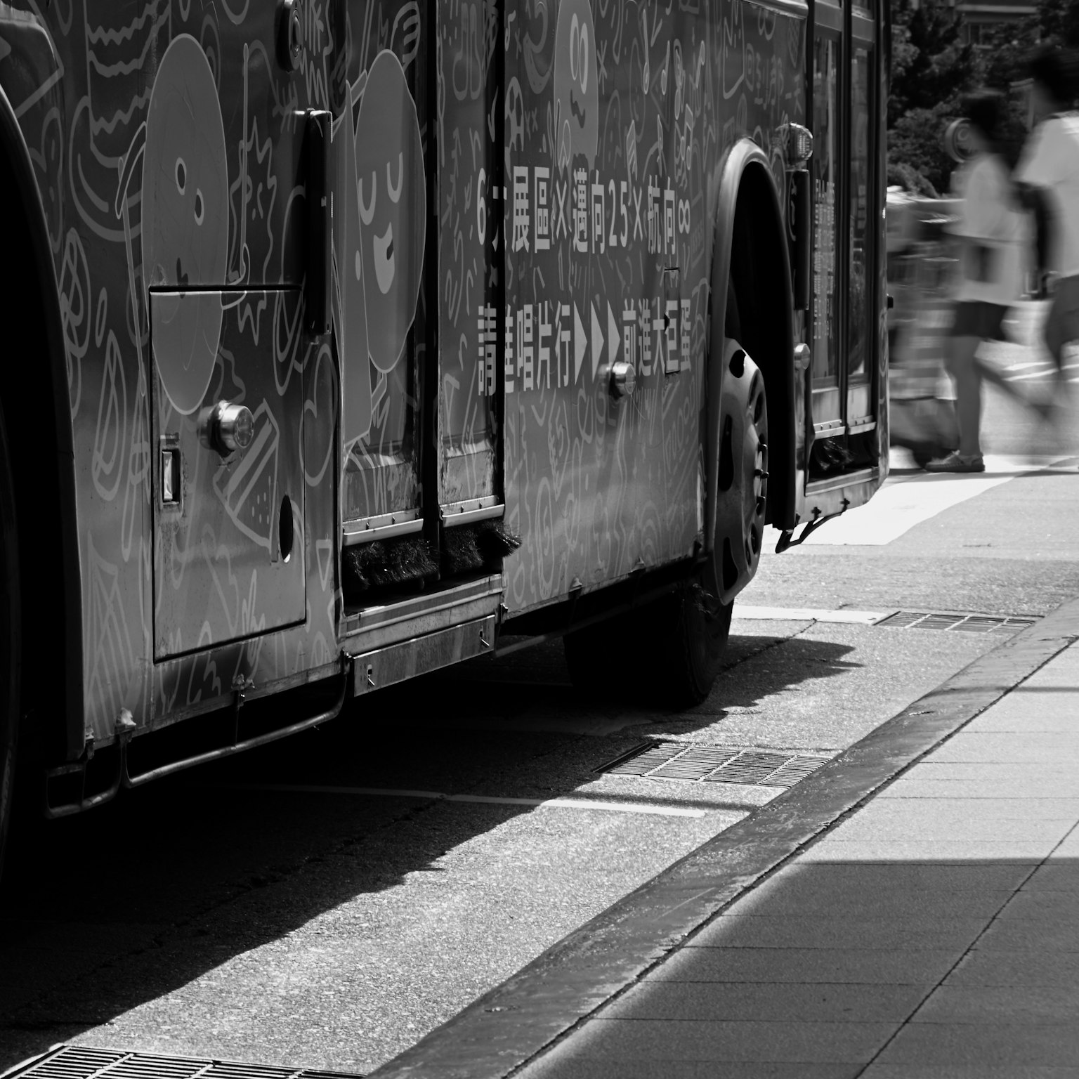Black and white image of a bus side with artistic designs and people walking
