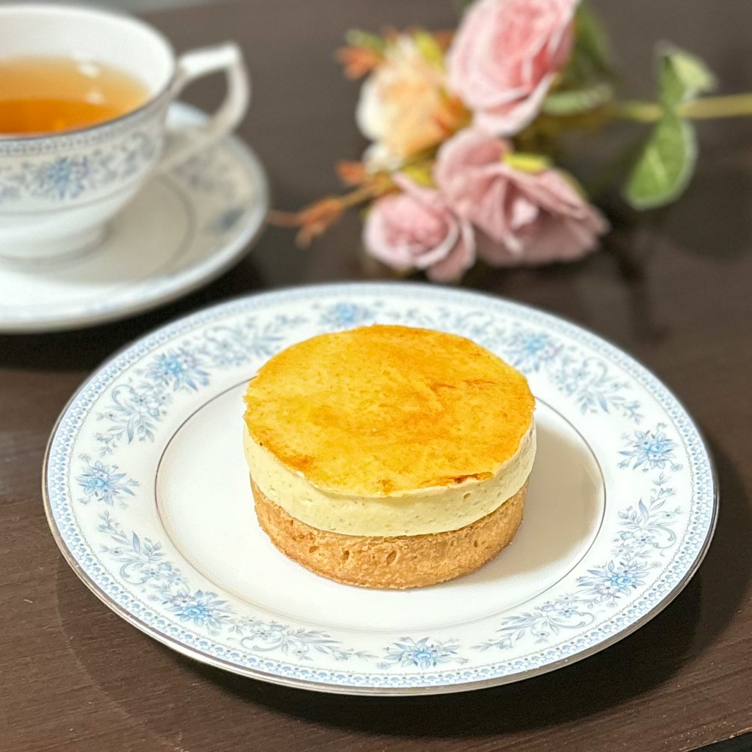 Un dolce elegantemente impiattato su un piatto decorativo con una tazza di tè e fiori