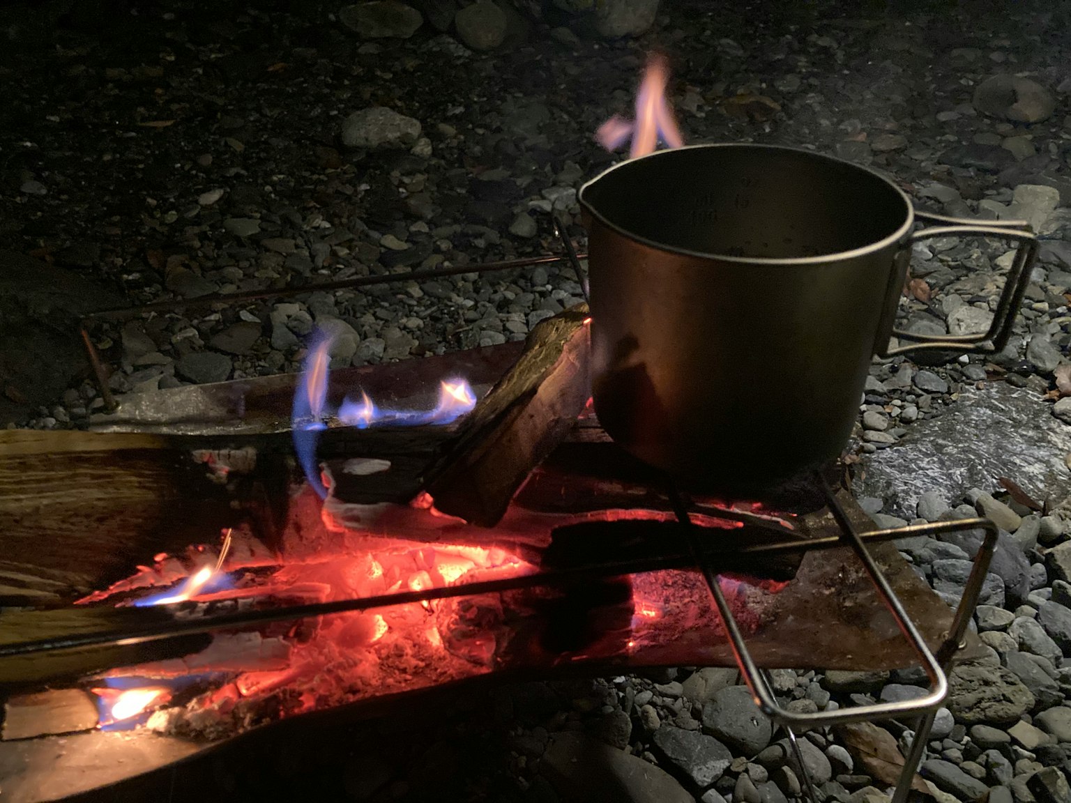 Pentola metallica sopra un fuoco da campeggio con fiamme e brace