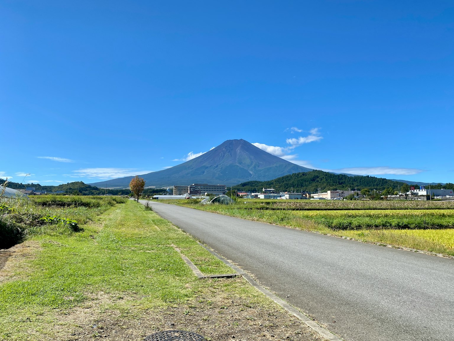 ภูเขาฟูจิที่สูงตระหง่านใต้ท้องฟ้าสีฟ้ากับภูมิทัศน์ชนบทโดยรอบ