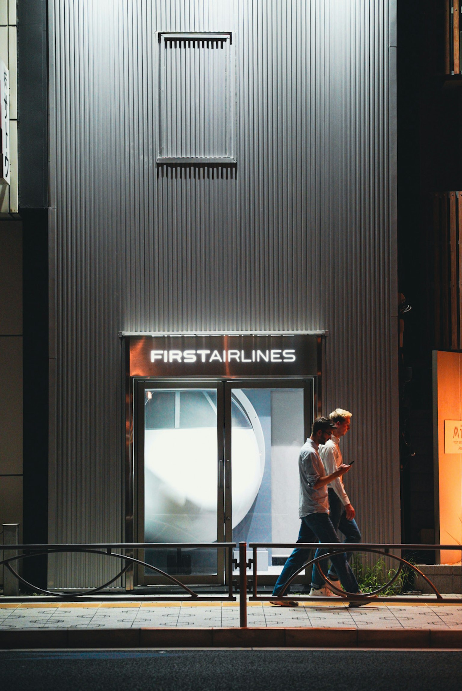 Zwei Männer, die nachts vor dem Schild FIRSTARLINES gehen