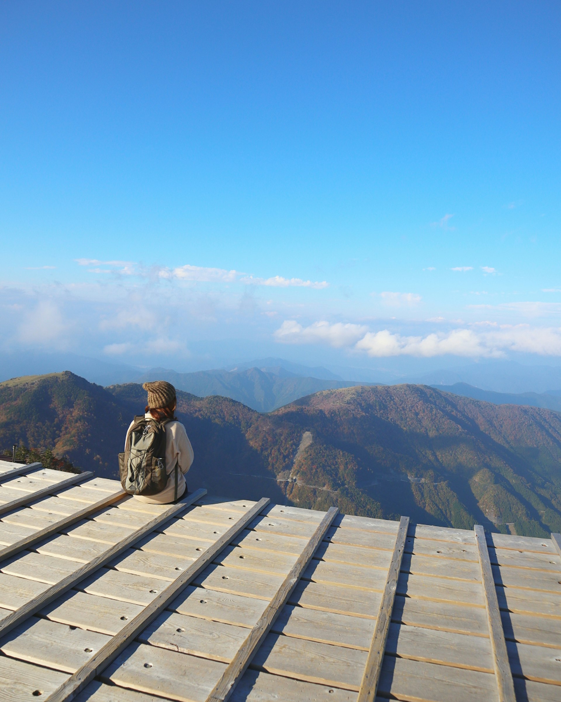 雲の広がる山頂の展望台で景色を見つめる登山者の後ろ姿