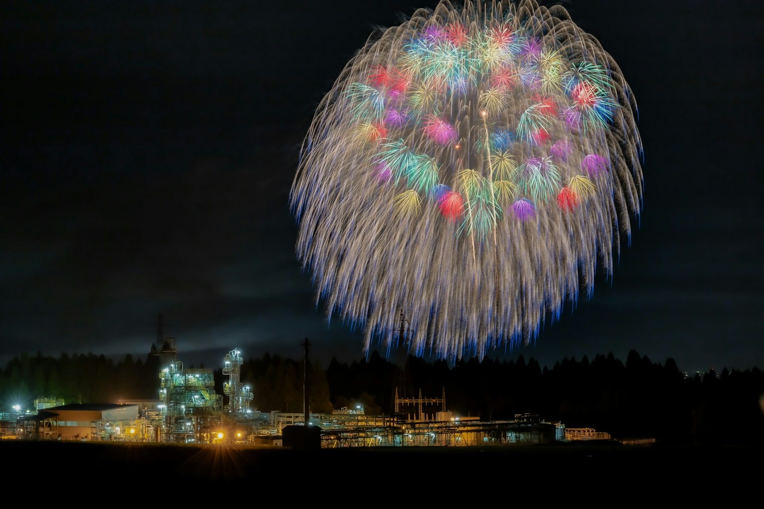 Fuegos artificiales coloridos estallando en el cielo nocturno sobre una instalación industrial