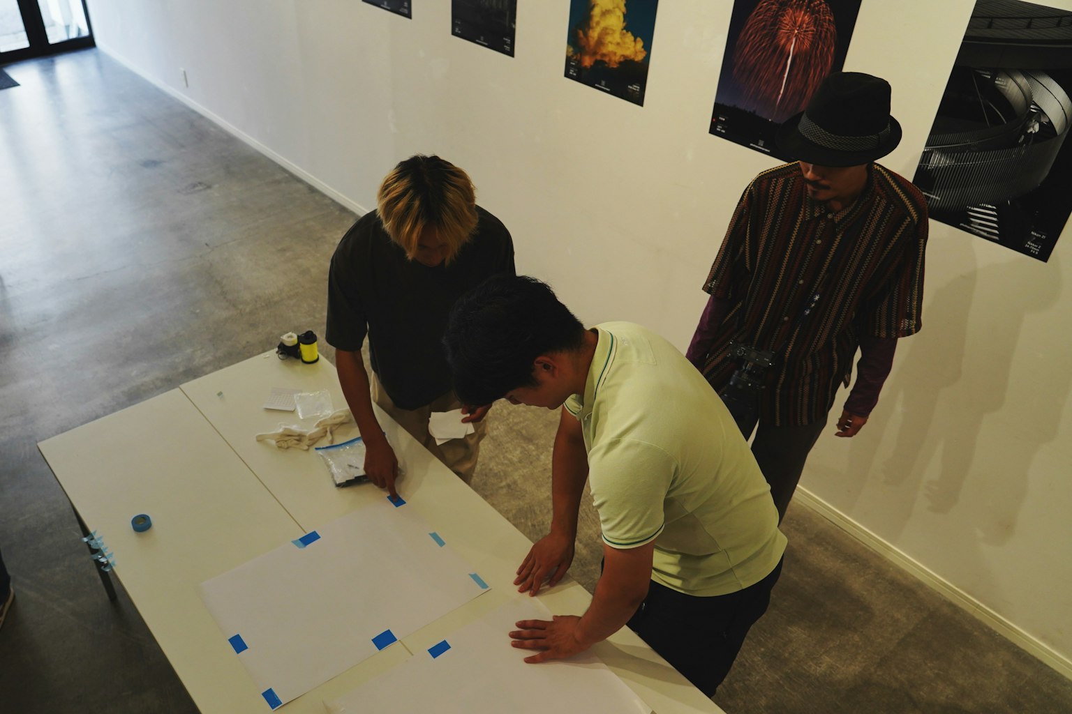 Tiga orang bekerja di meja dalam pengaturan studio seni