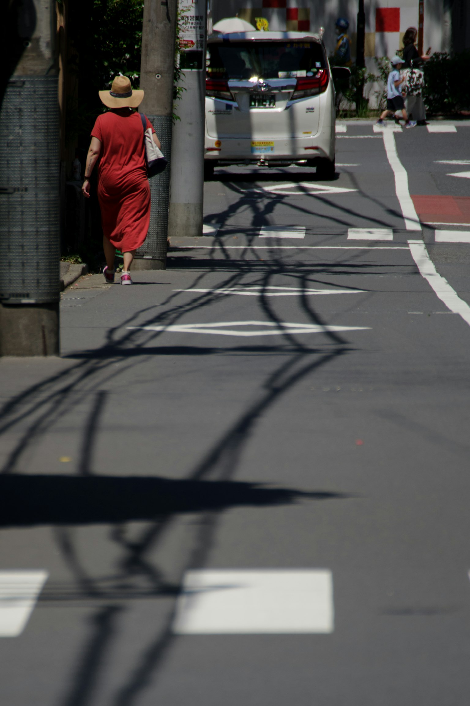Eine Frau in einem roten Kleid geht die Straße entlang mit Schatten von Stromleitungen auf dem Gehweg
