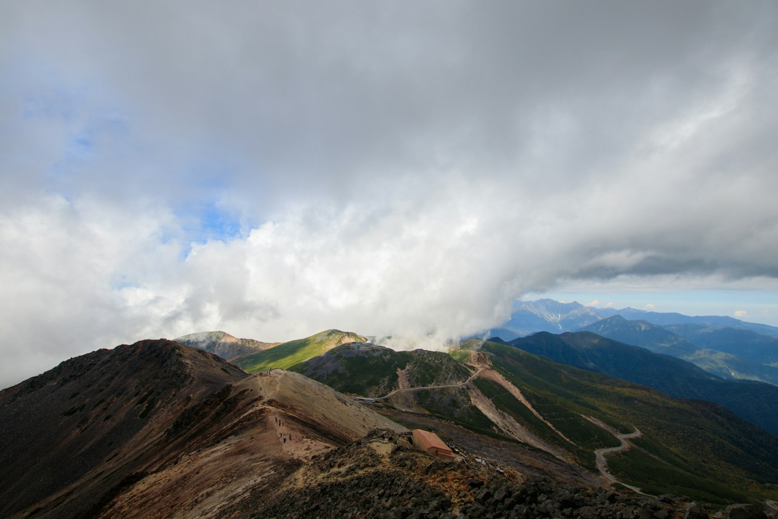 View from a mountain peak with clouds and green hills visible