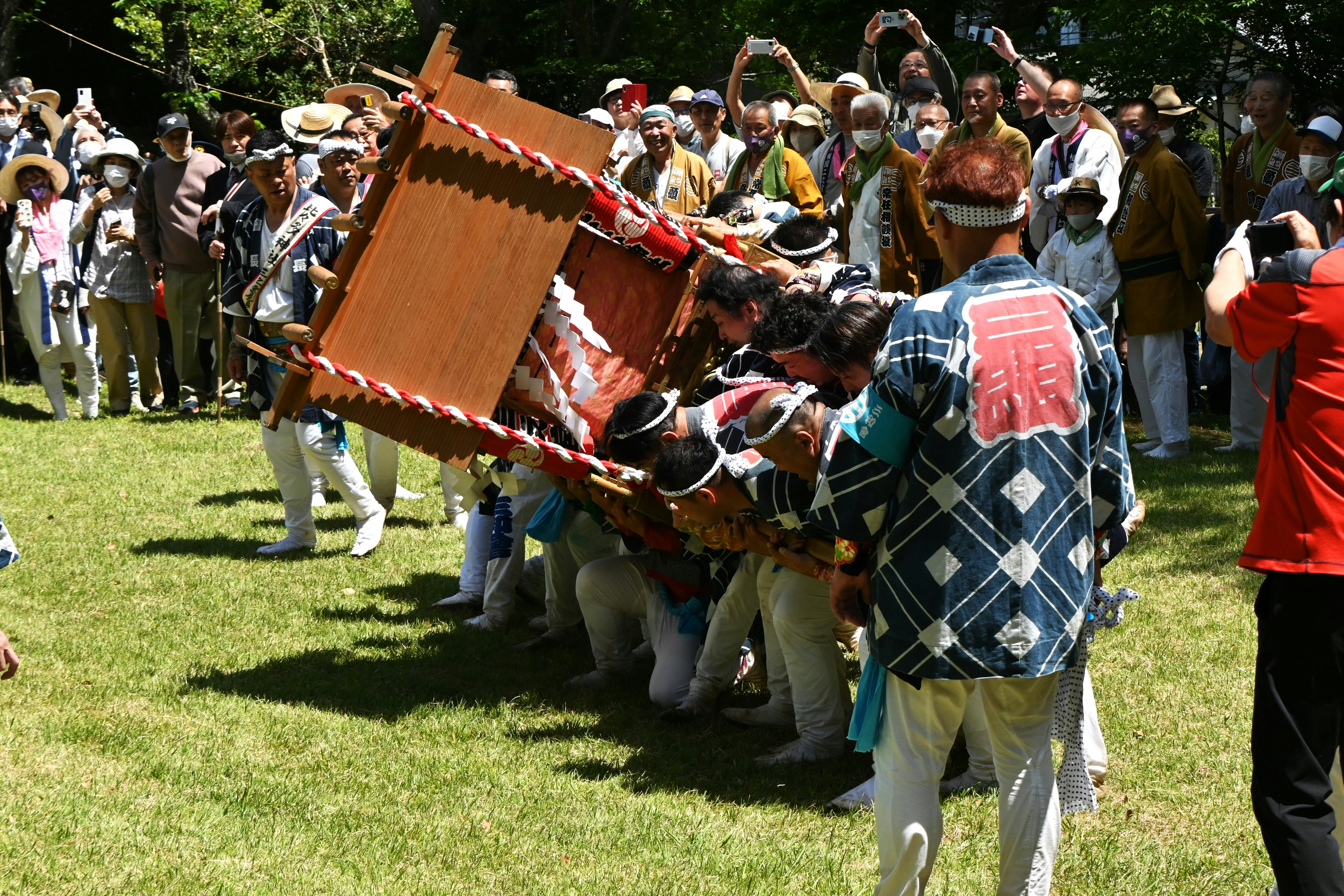 草地で担がれる太鼓と祭りの行列