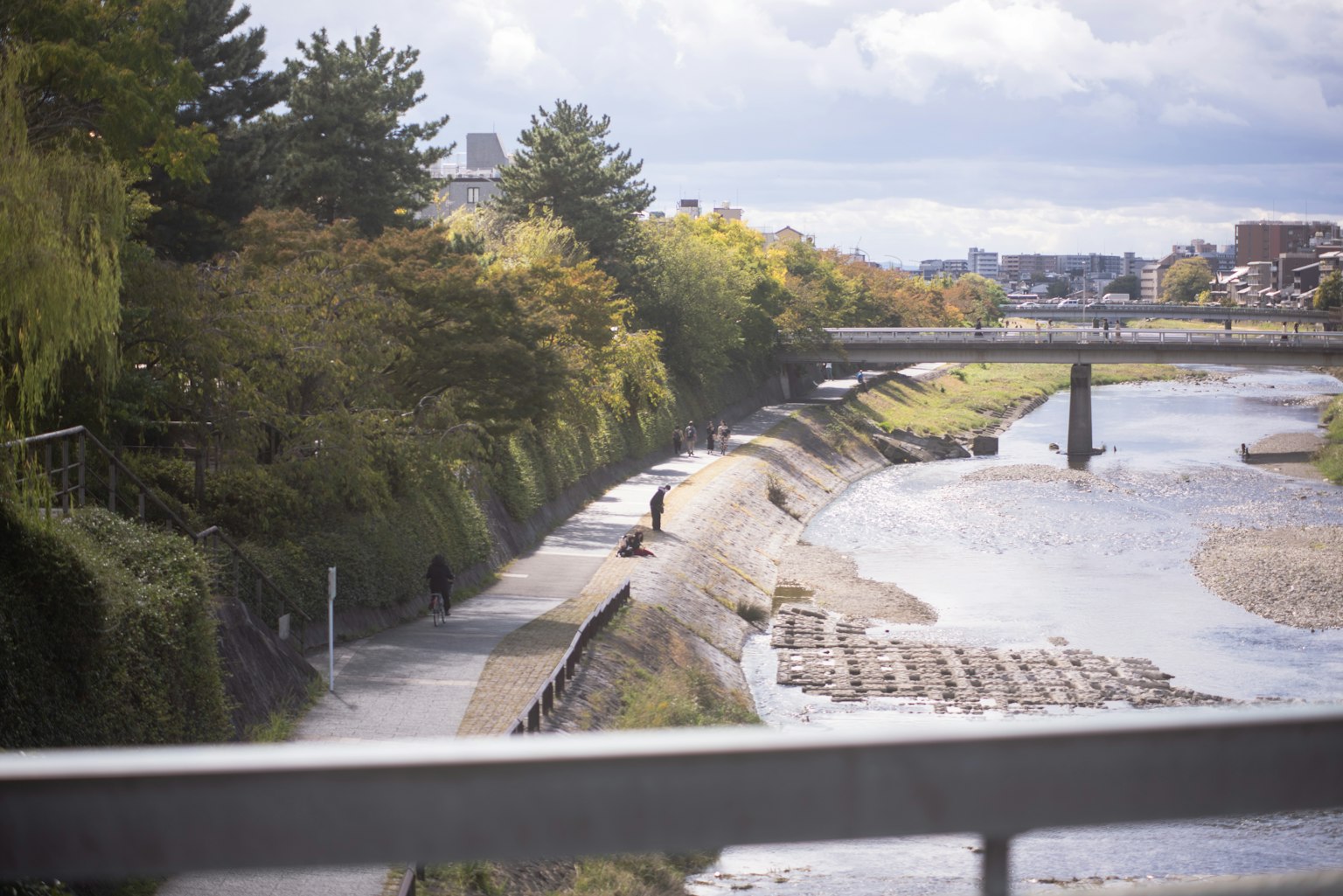 People walking along a riverside path with autumn trees