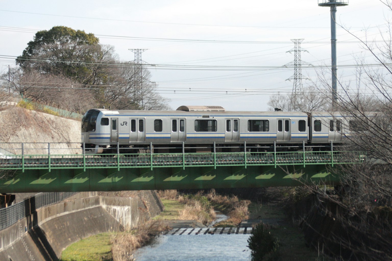 Train traversant un pont vert au-dessus d'une rivière avec des lignes électriques en arrière-plan