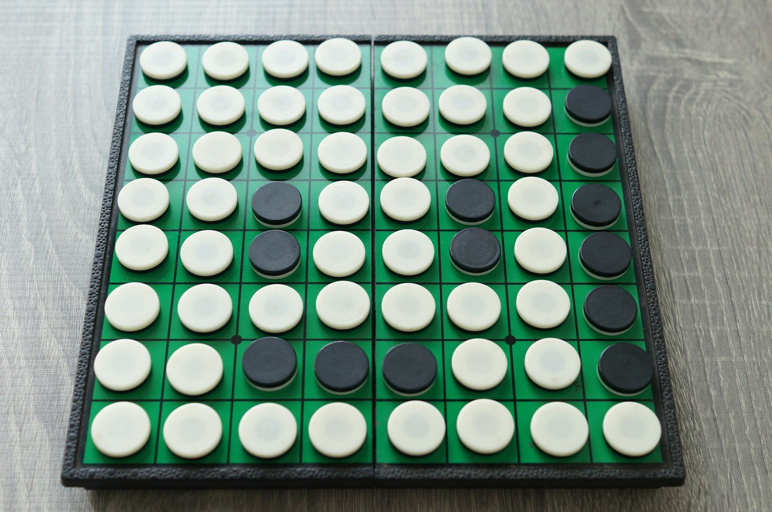 ชิ้นส่วนเกม Othello ที่จัดเรียงเป็นสีดำและขาวบนกระดานสีเขียว