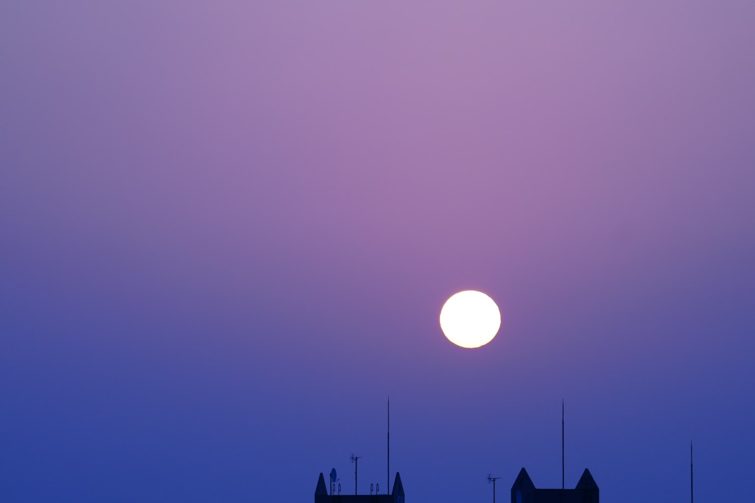 Sole grande in un cielo viola con edifici in silhouette