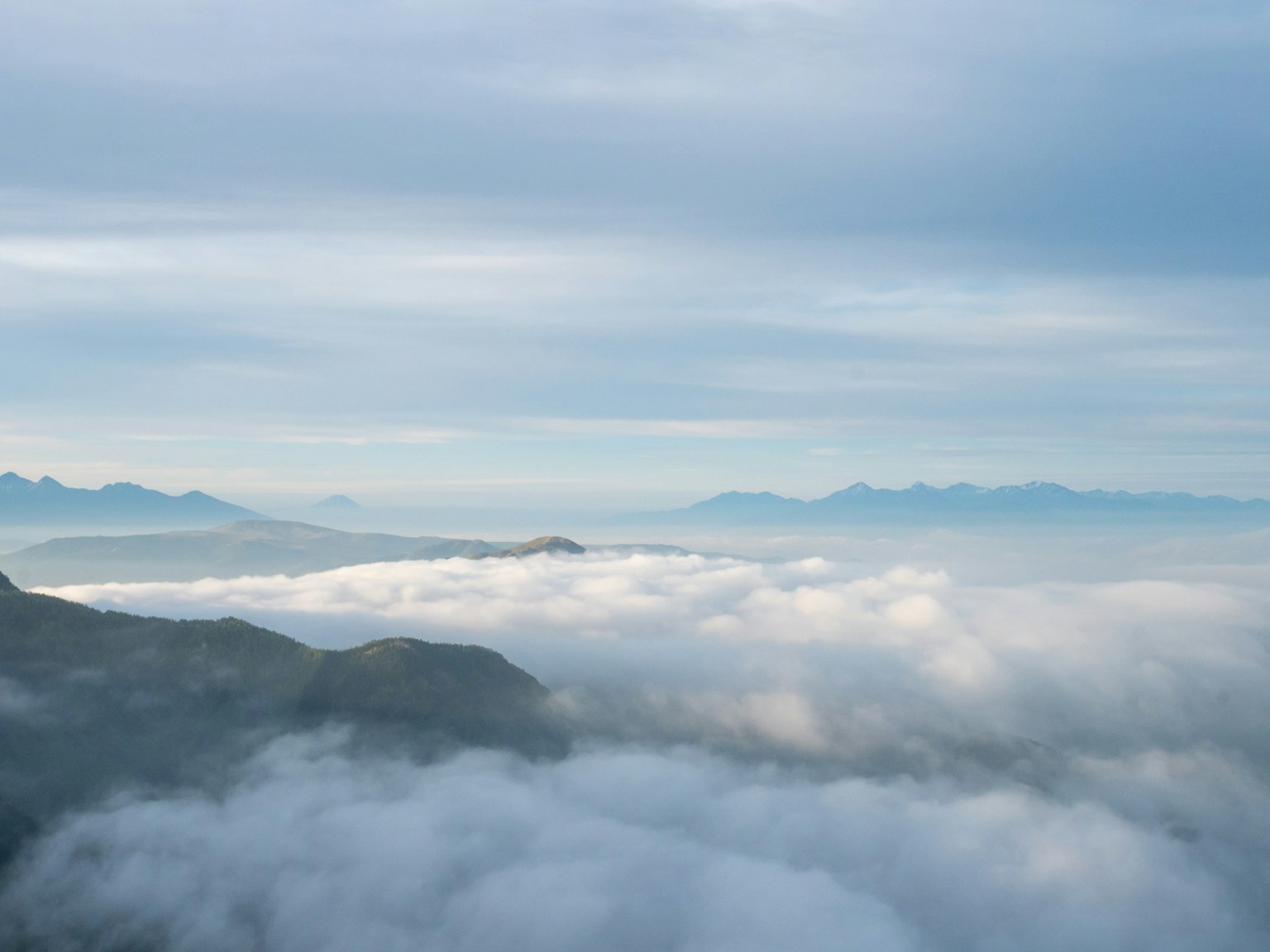 Un paisaje de montañas con un mar de nubes bajo un cielo azul
