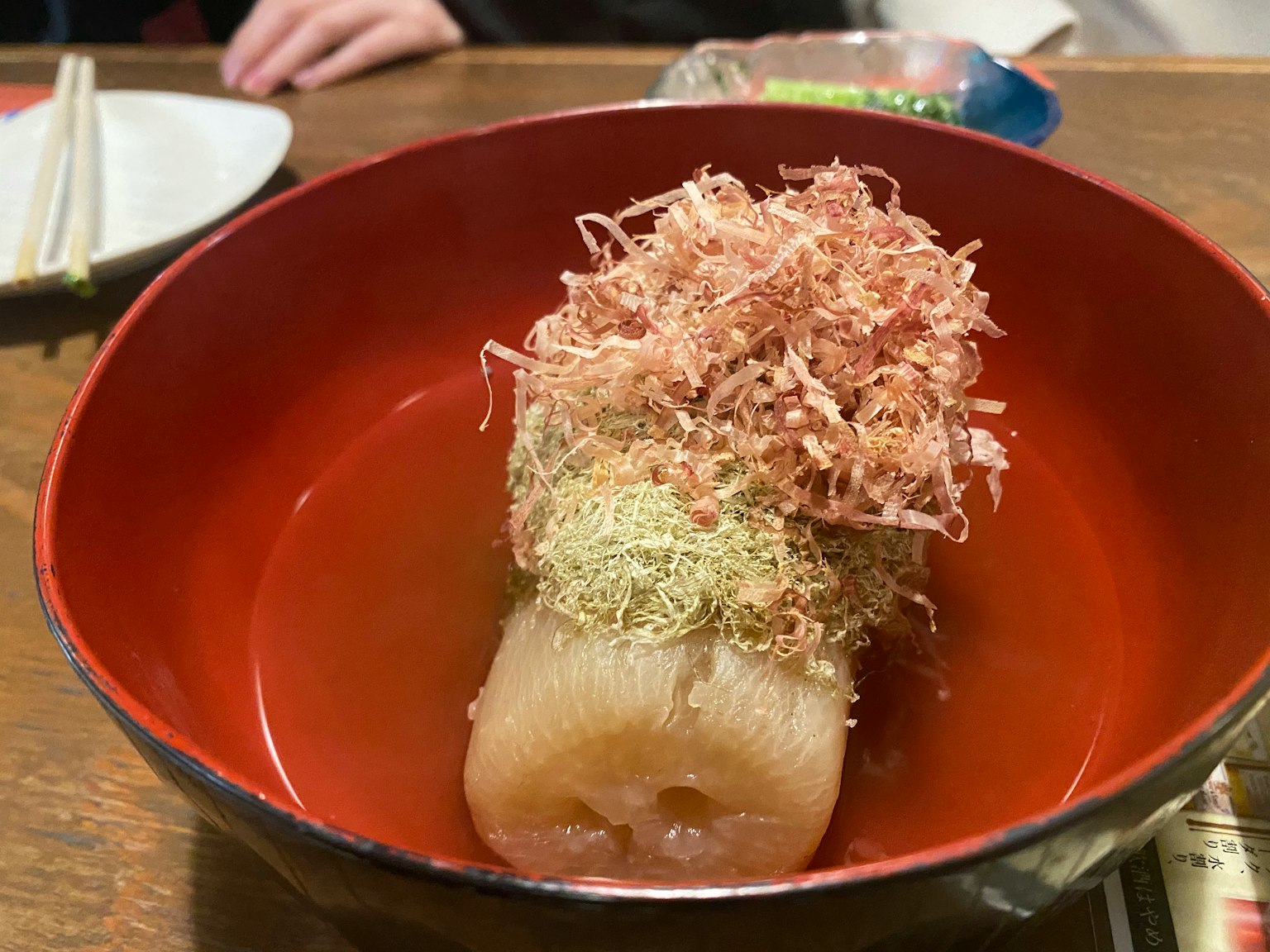 Japanese dish featuring daikon topped with bonito flakes and aonori in a red bowl