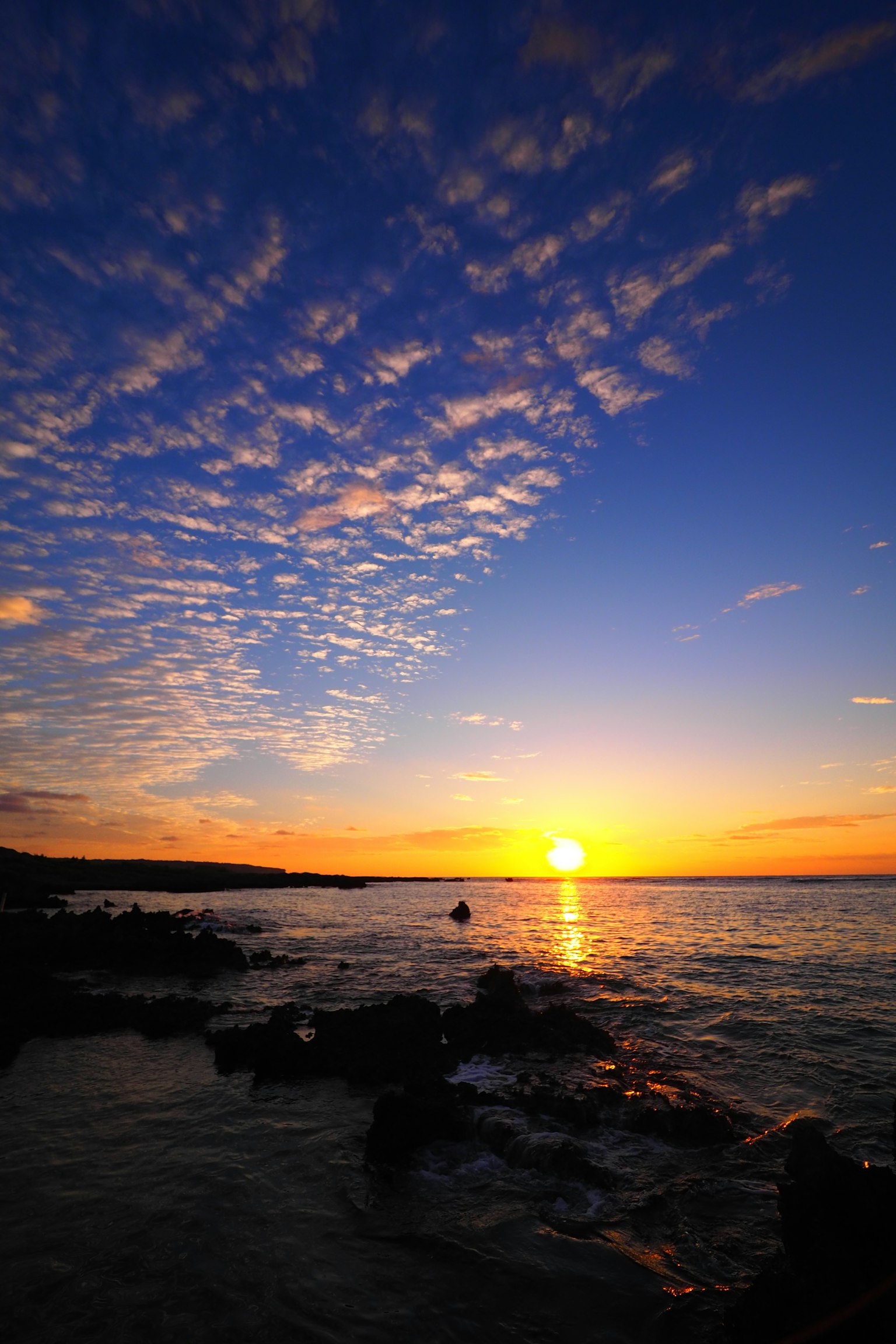 A beautiful sunset over the ocean with a blue sky and orange clouds