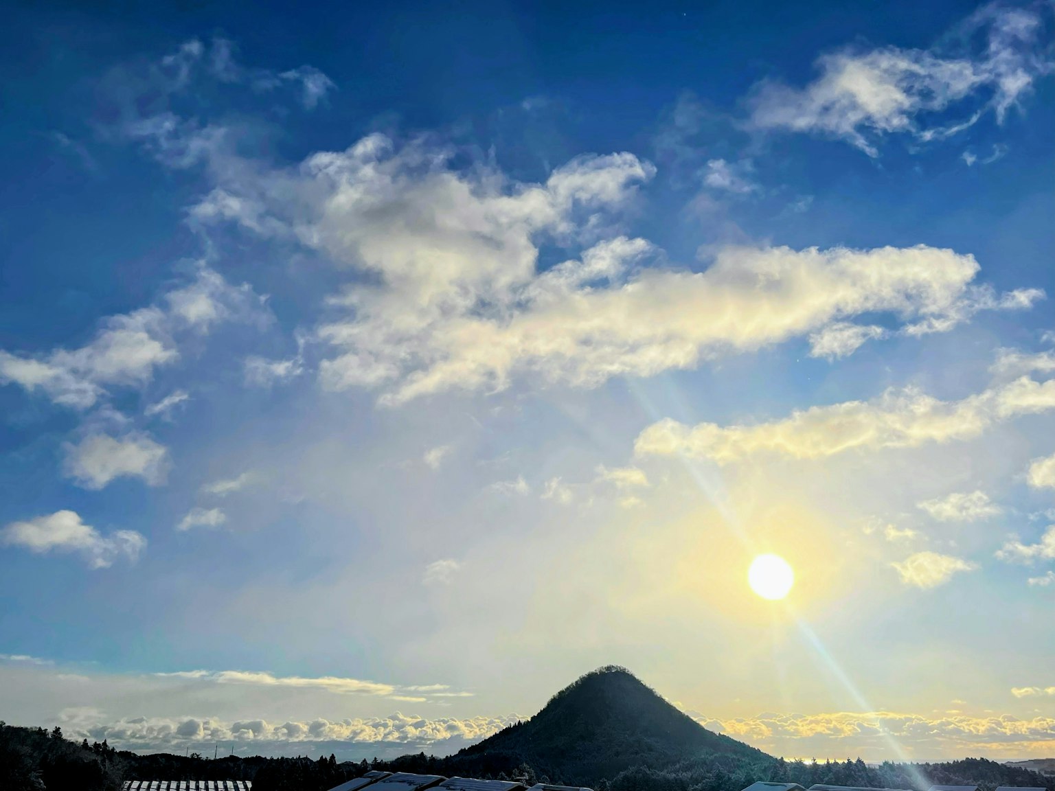 Landscape featuring a mountain and sun under a blue sky with white clouds