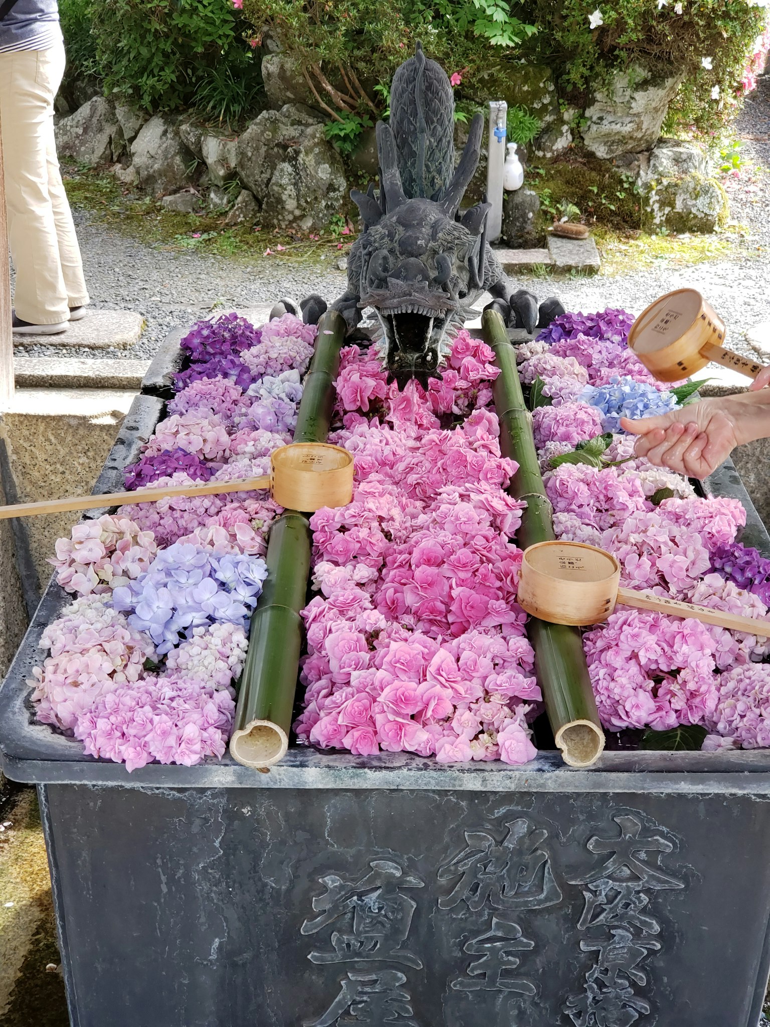 A shallow basin at a shrine filled with colorful flowers and bamboo water spouts