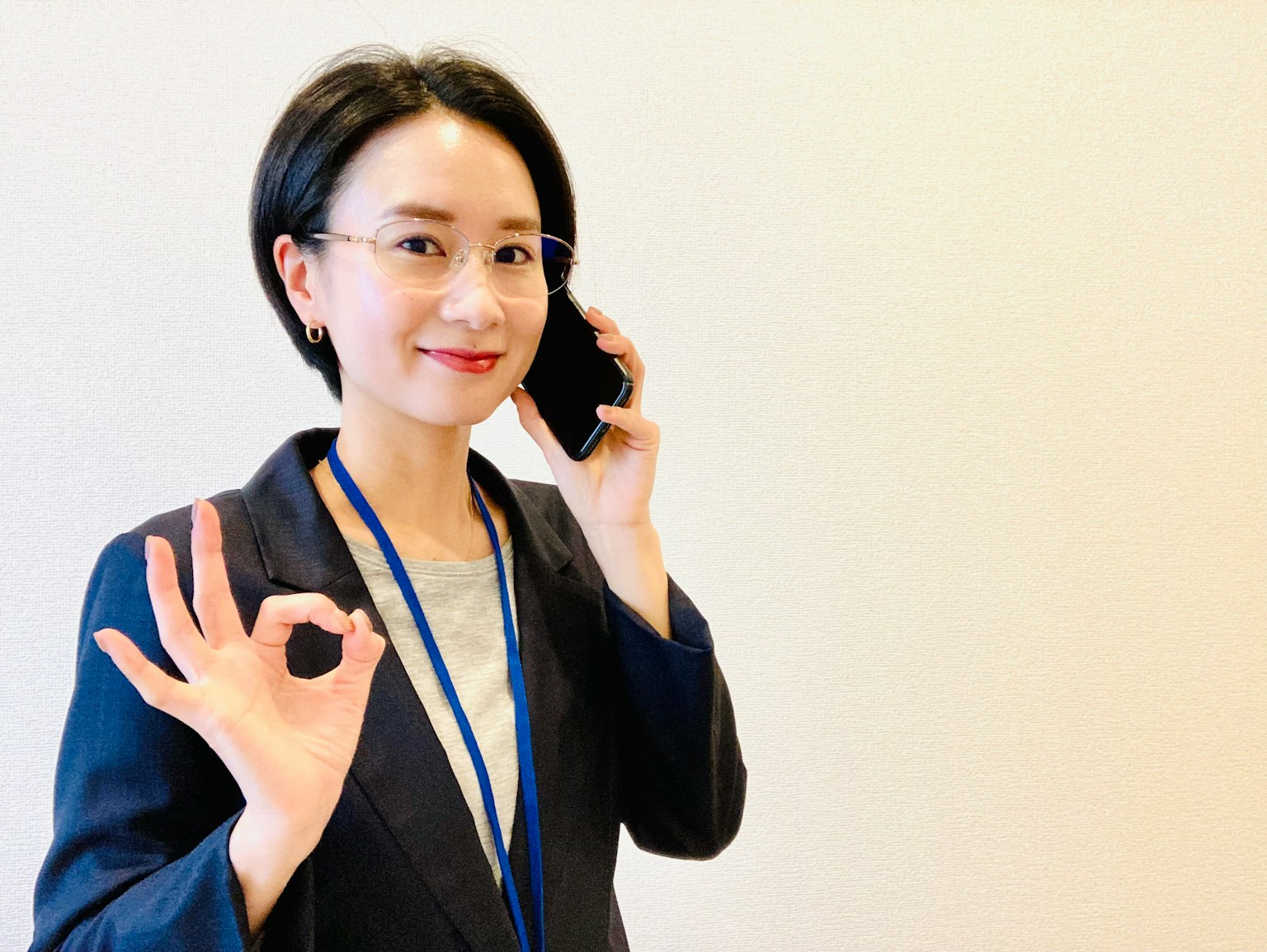 Frau im Business-Outfit mit Telefon und Okay-Geste