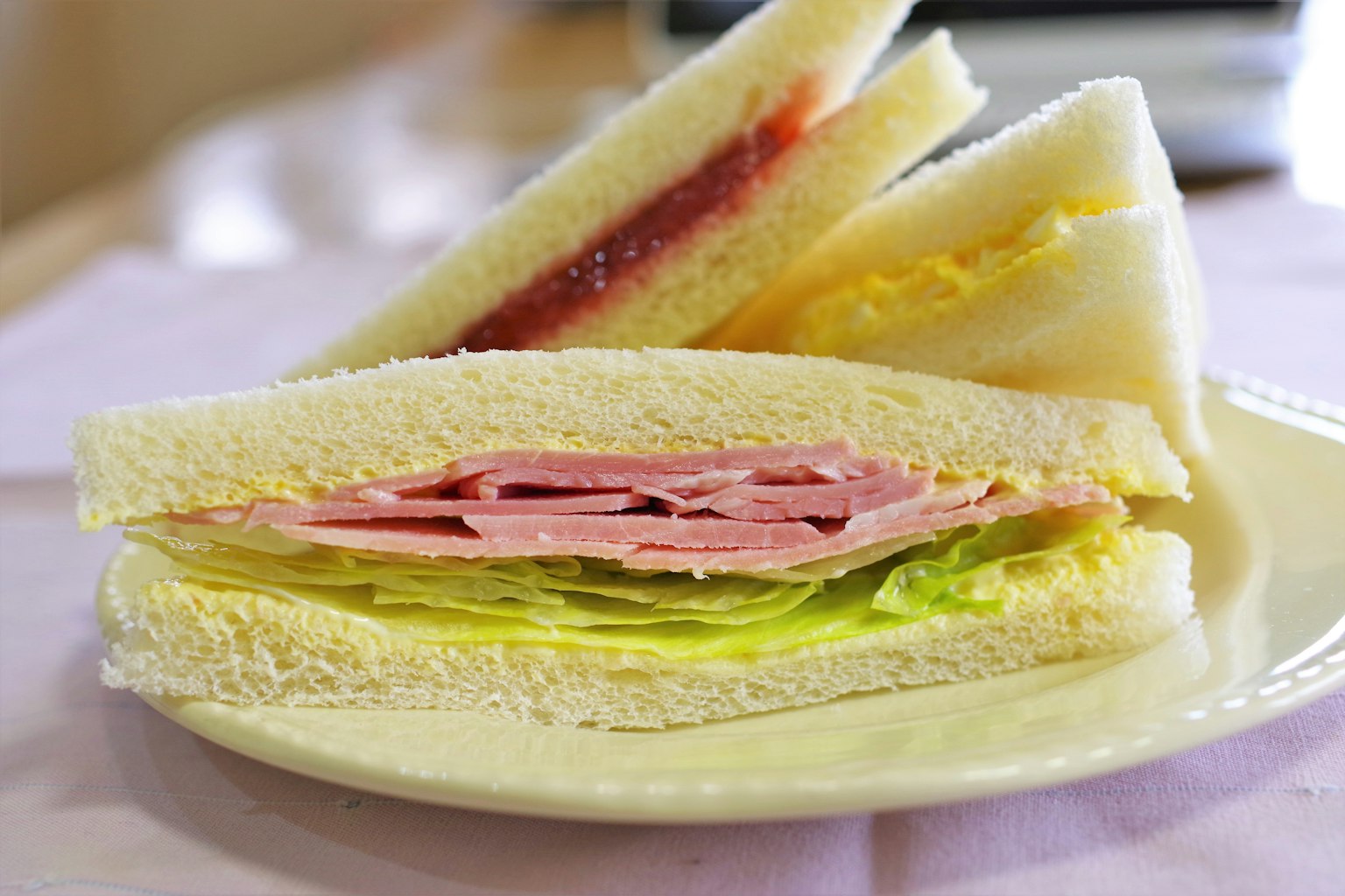 Un piatto con panini a strati contenenti prosciutto, lattuga e marmellata