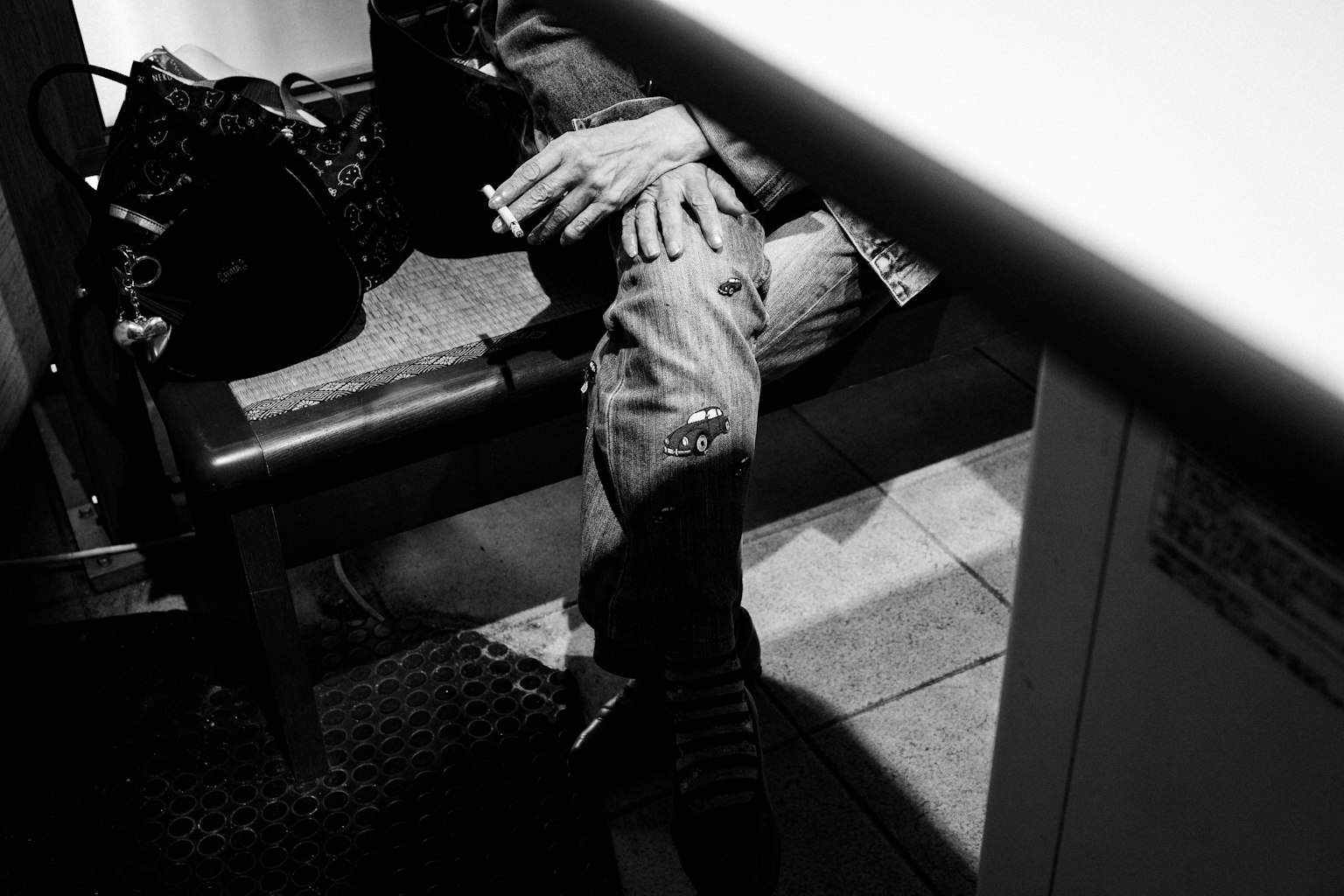 Black and white photo of a person sitting on a bench holding a cigarette