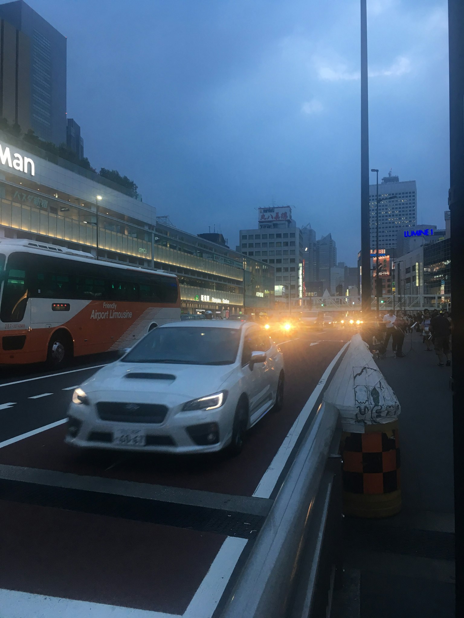 어두워지는 도시 거리에서 흰색 차량이 운전 중 버스와 고층 빌딩이 근처에 있음