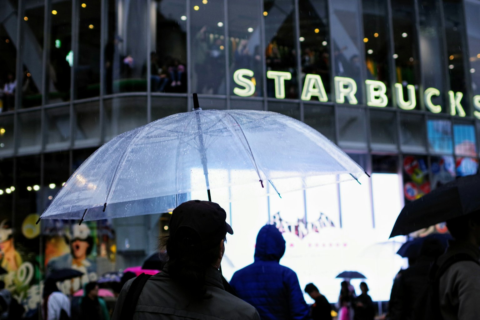 Menschen mit einem transparenten Regenschirm vor einem Starbucks in der Nacht