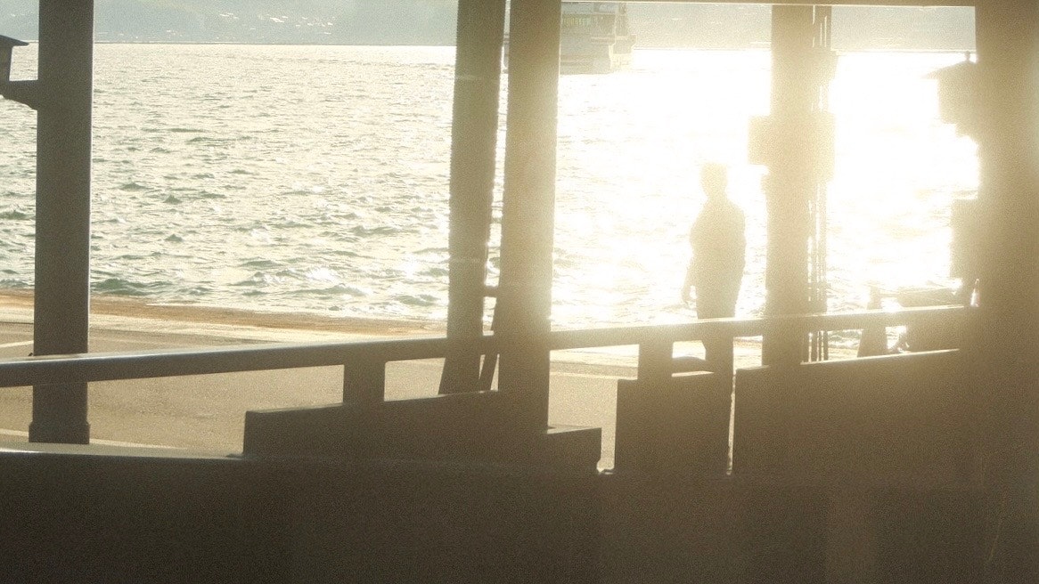桟橋の手すり越しに海を見つめる男性のシルエットと夕日