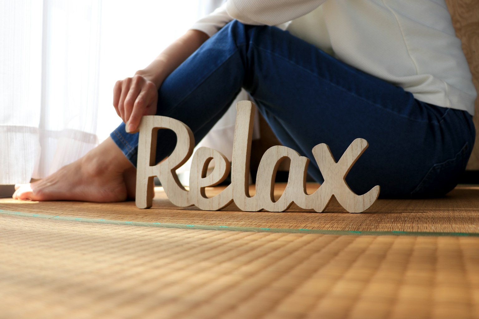Person holding a wooden sign that says Relax with feet resting on tatami mat