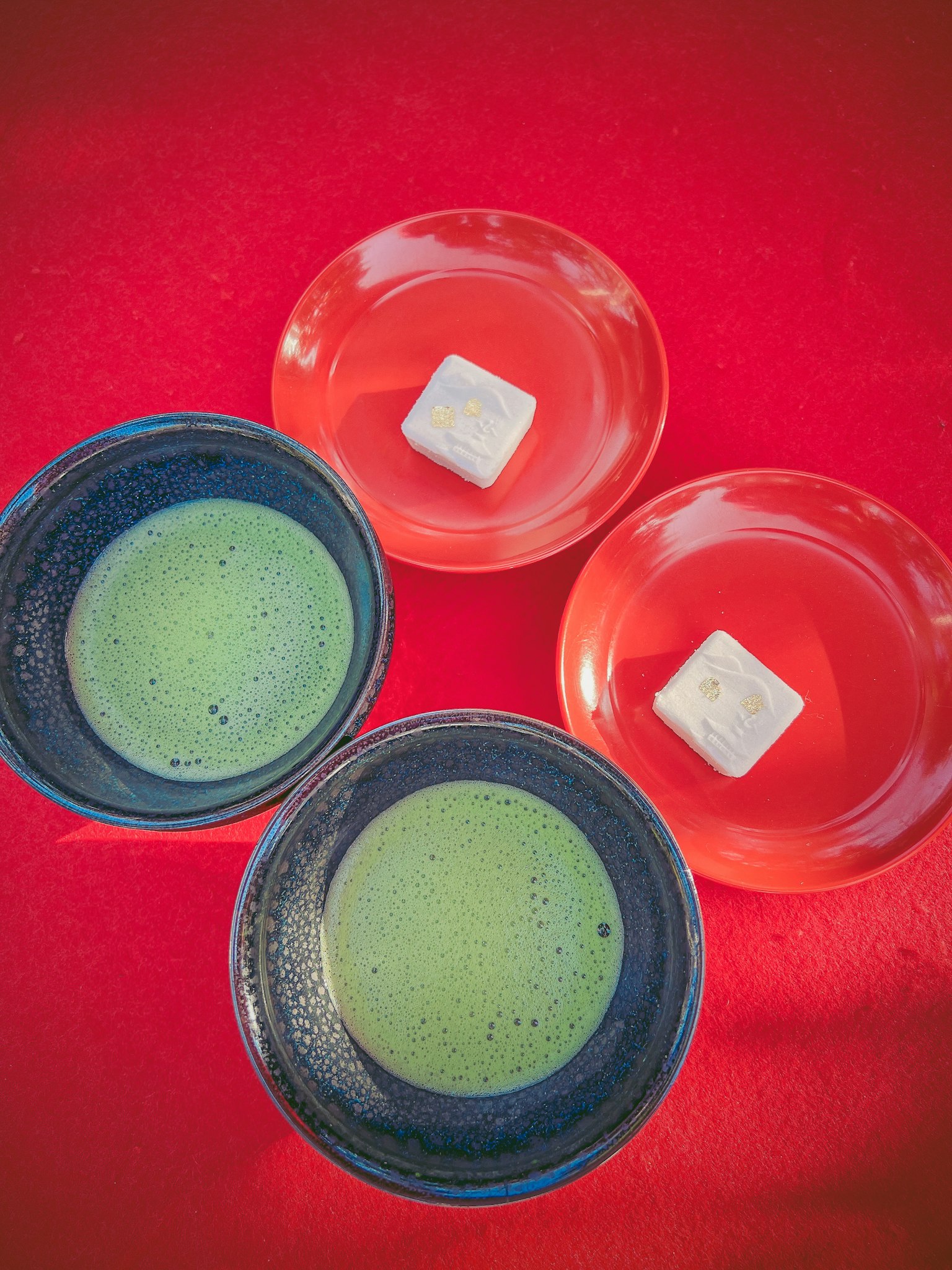 Two green matcha bowls and two orange plates on a red background