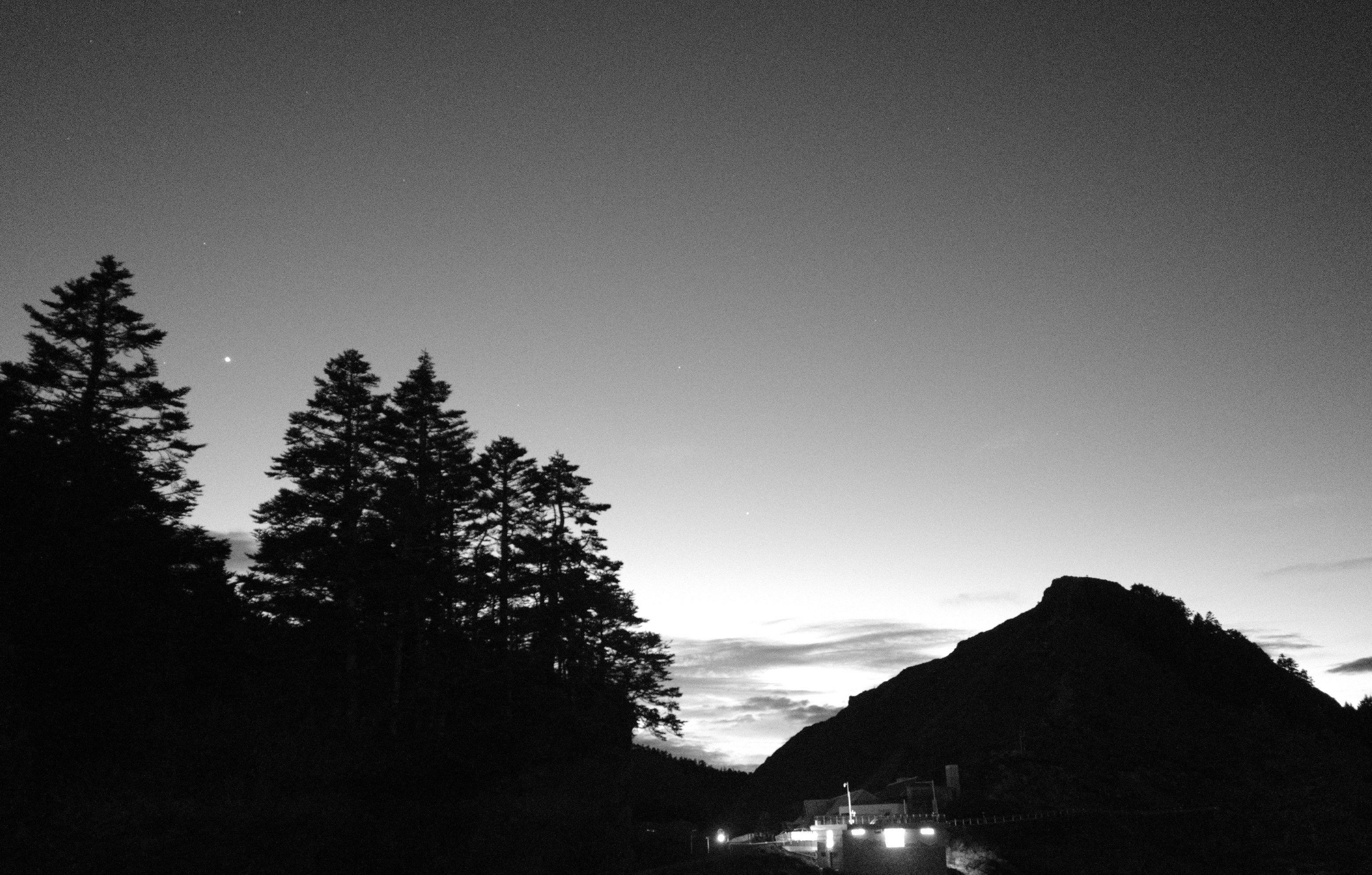 山の稜線と木々のシルエットが広がる夜の道路風景
