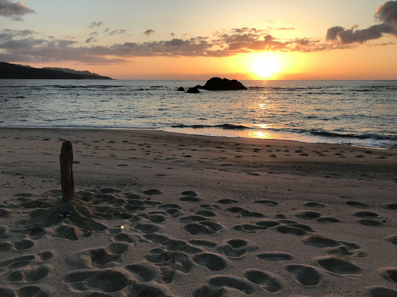 Scène de plage avec coucher de soleil sur l'océan et empreintes dans le sable