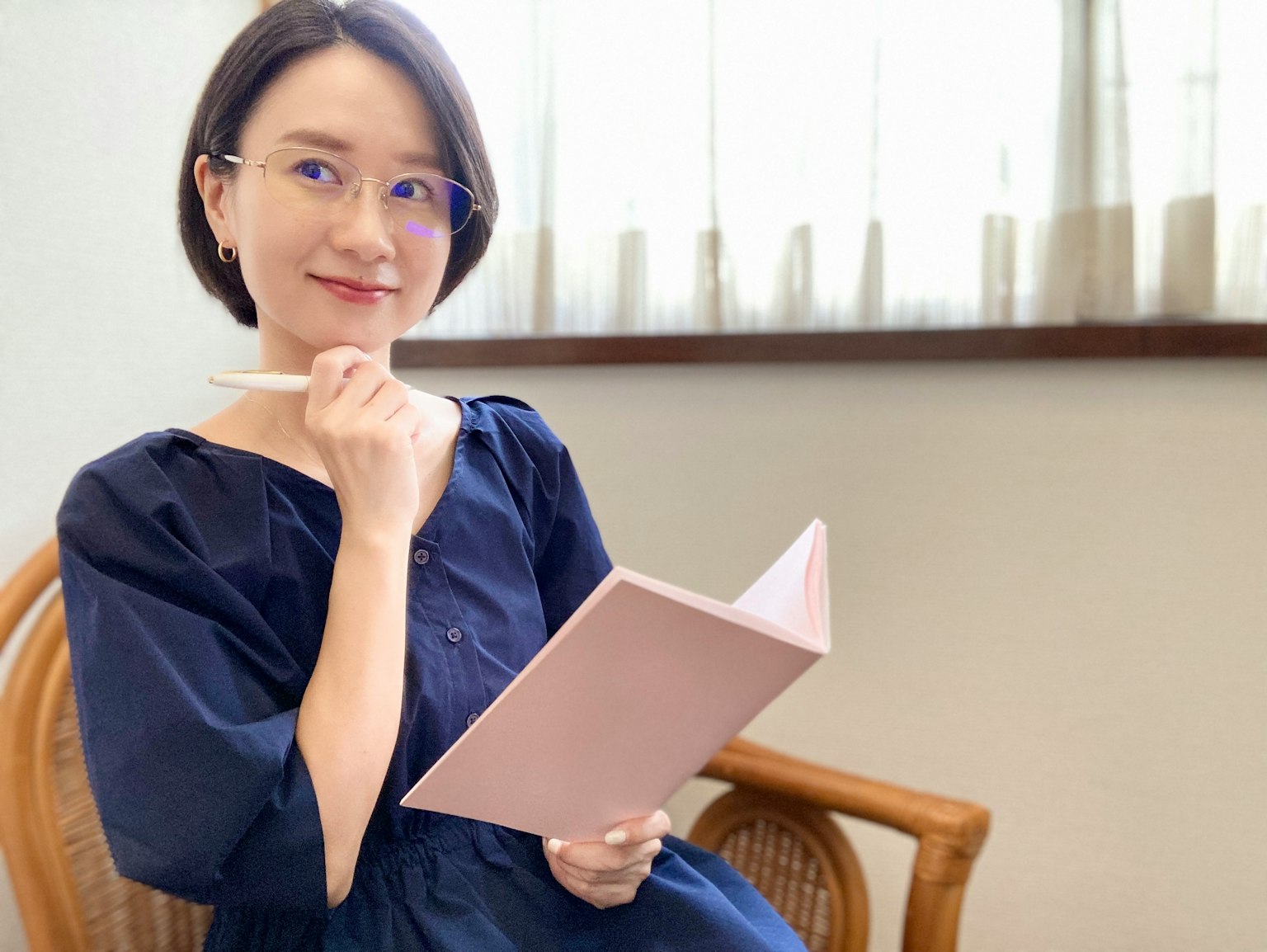 Người phụ nữ cầm sổ tay màu hồng và bút đang suy nghĩ trong nhà