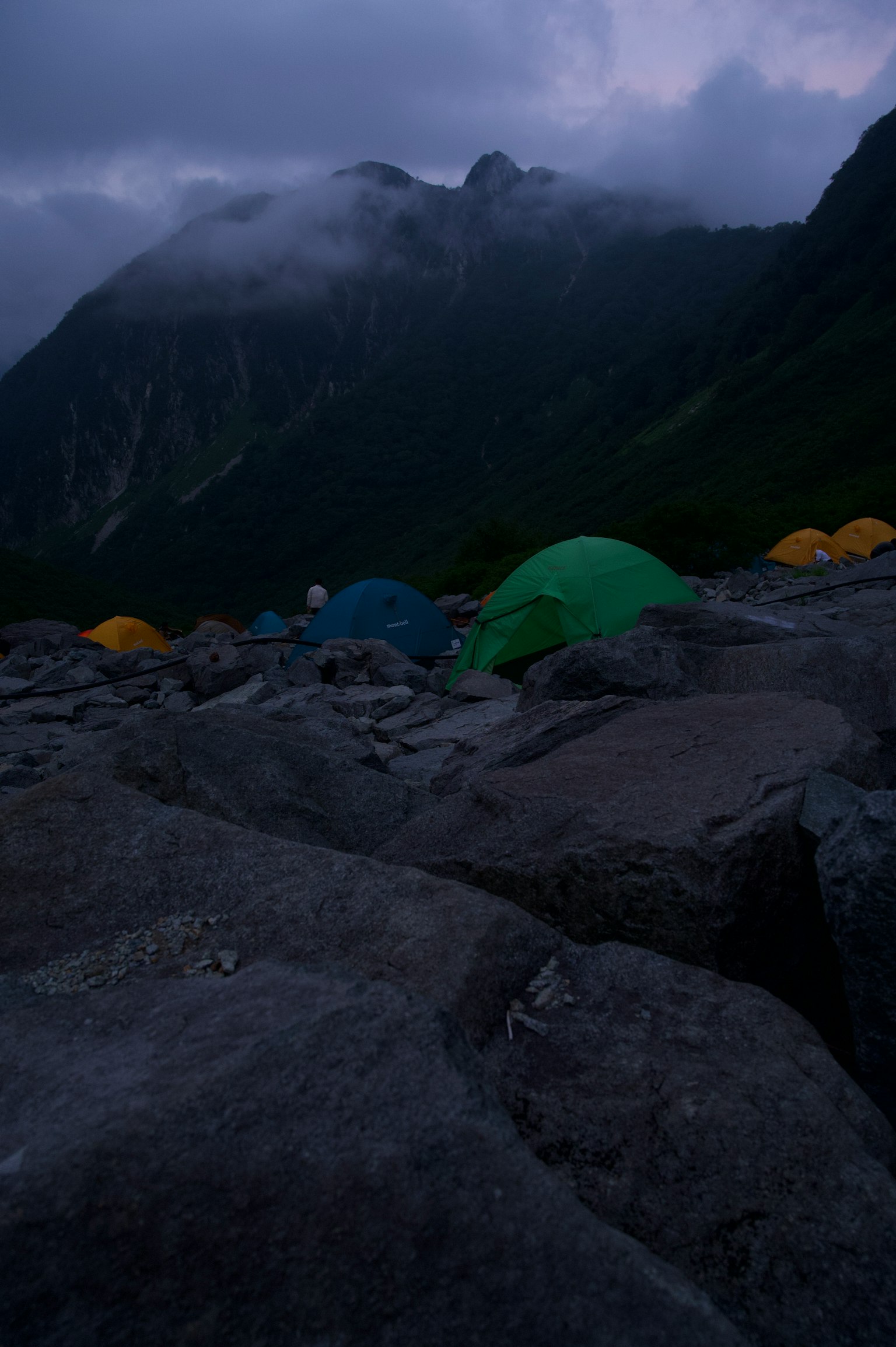 夜景中绿色和黄色帐篷与雾蒙蒙的山脉相映衬