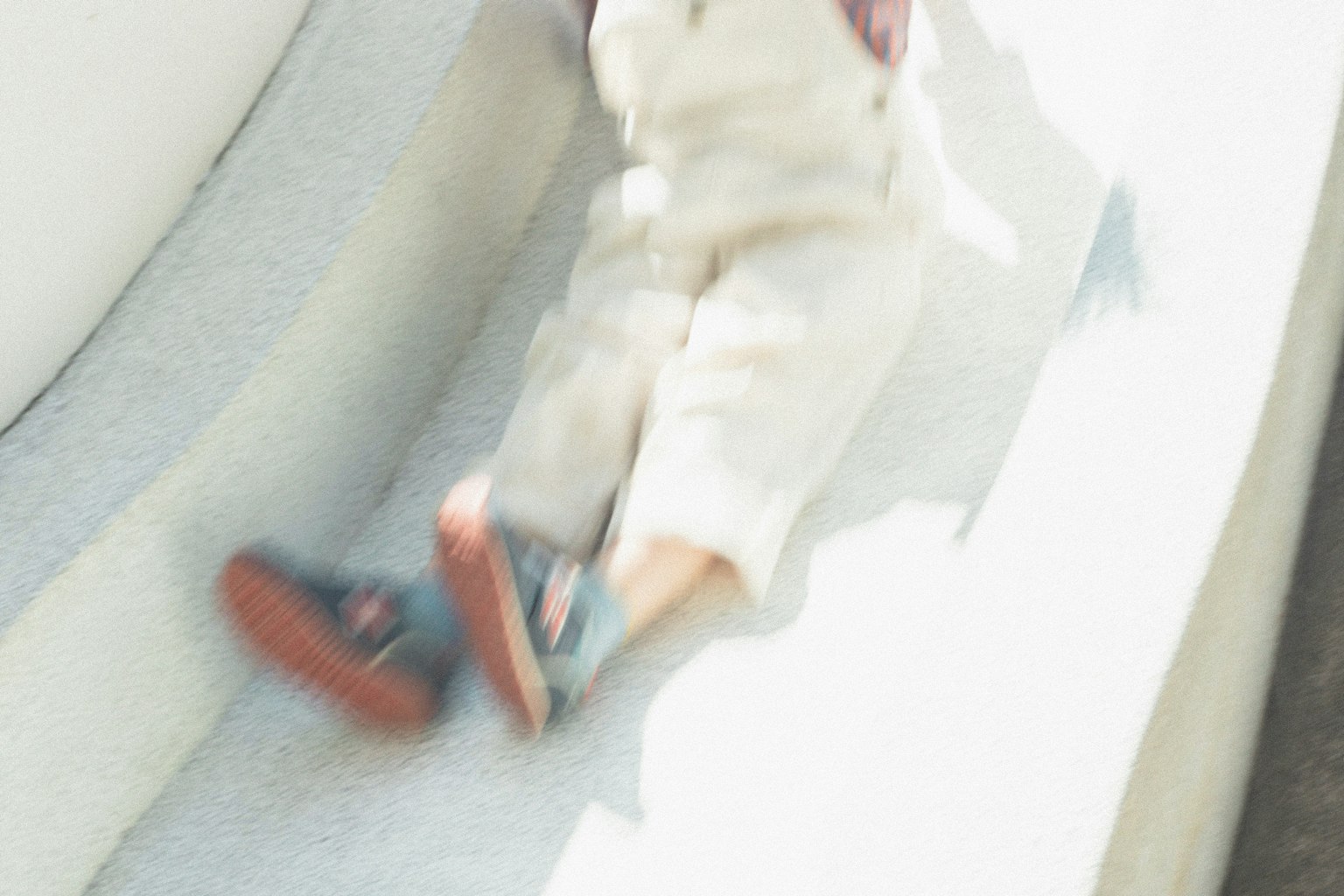 Ein Kind rutscht eine Rutsche hinunter und trägt weiße Hosen und blaue Schuhe