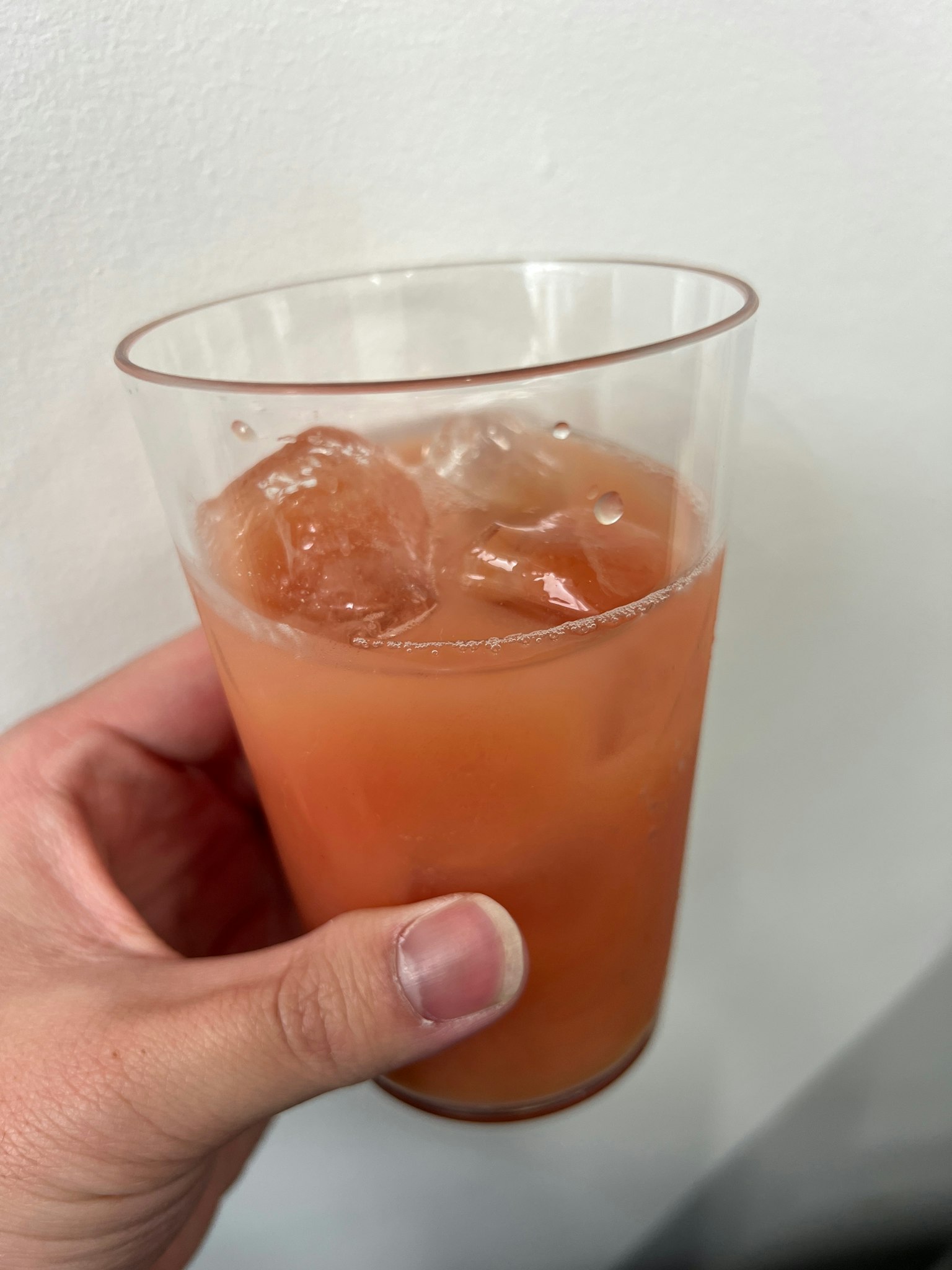 Une main tenant un gobelet transparent rempli d'une boisson orange avec des glaçons